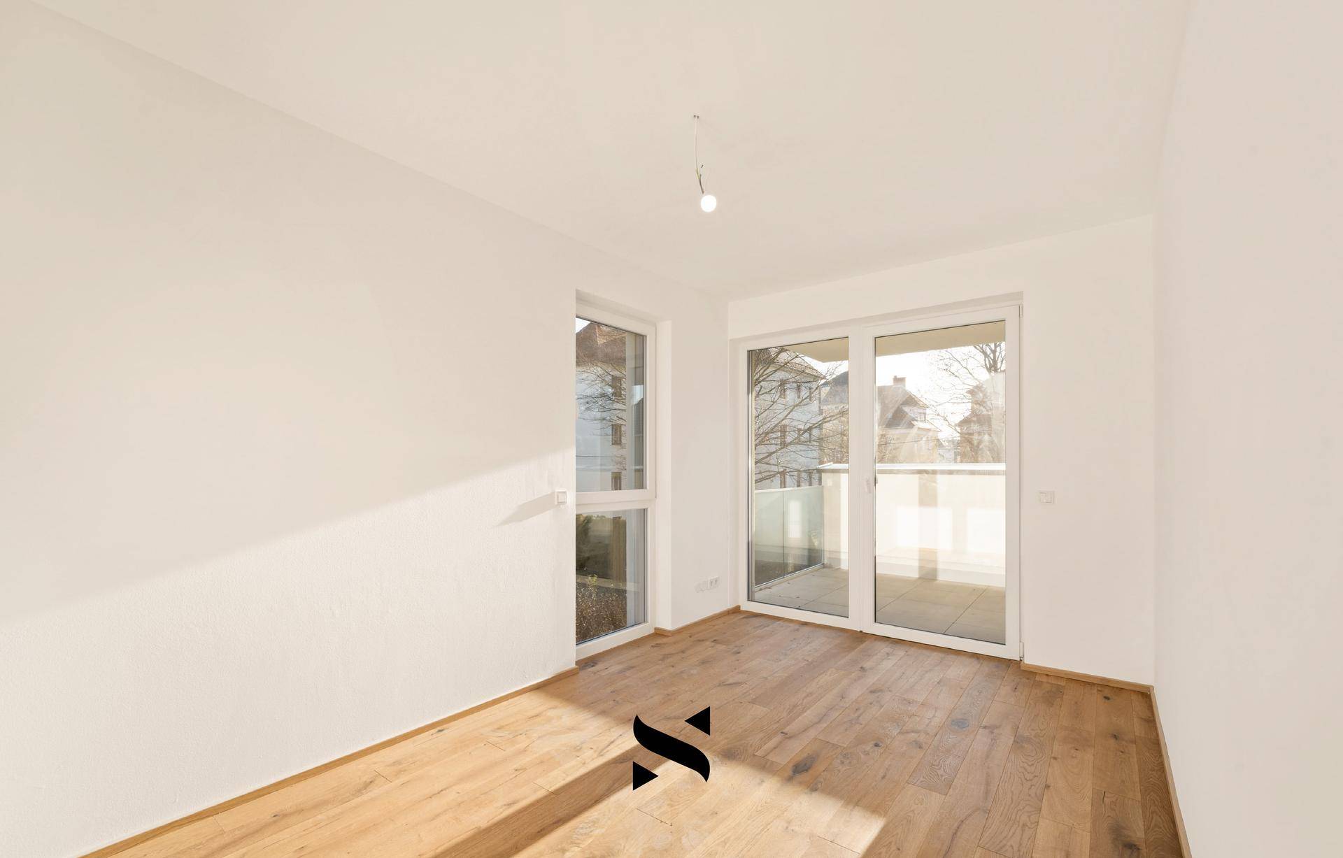 Helles Schlafzimmer mit Holzboden und großen Fenstern, die viel Licht hereinlassen.