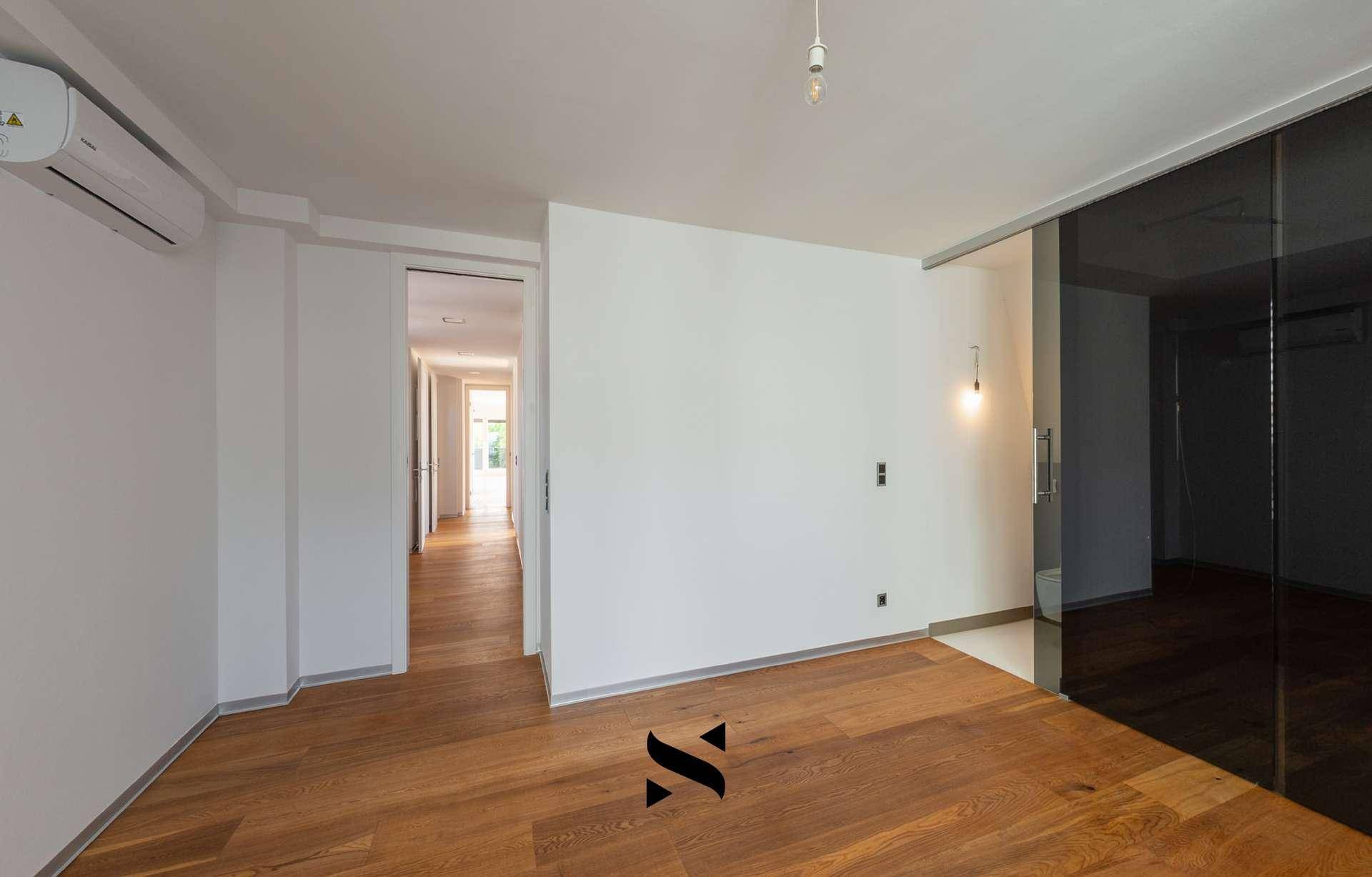 Geräumiges Zimmer mit Holzboden, Klimaanlage und Zugang zu einem weiteren Bereich.