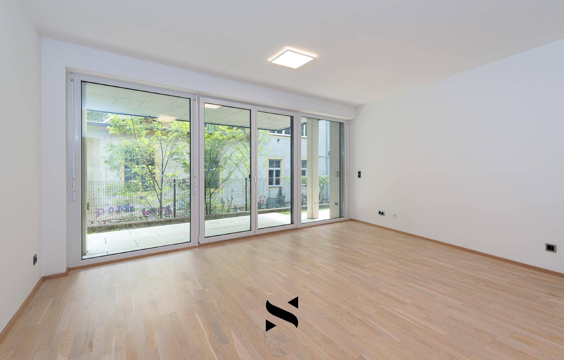 Helles, leeres Zimmer mit großen Schiebetüren und hellem Parkettboden, ideal für ein Wohnzimmer.