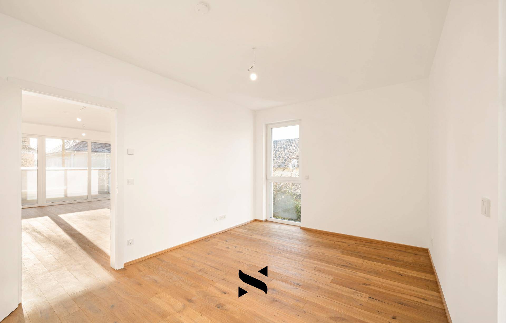Helles Zimmer mit Holzboden und Zugang zum Wohnbereich, ideal als Schlafzimmer.