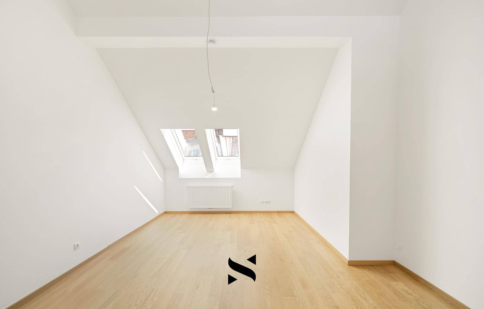 Helles Zimmer im Dachgeschoss mit Parkettboden, weißen Wänden und Dachfenstern.