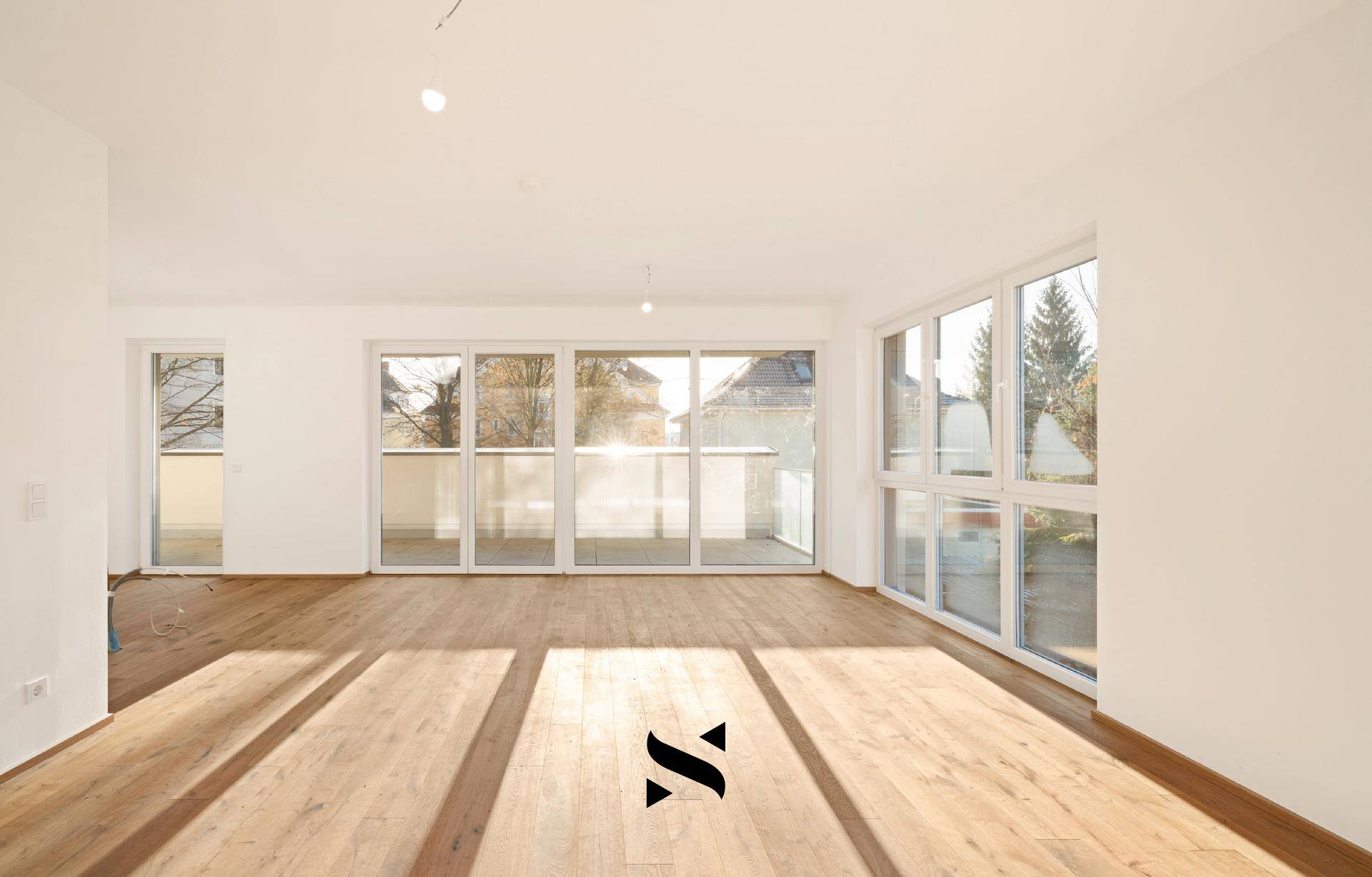 Geräumiges Wohnzimmer mit viel Tageslicht, Holzboden und breiter Fensterfront.