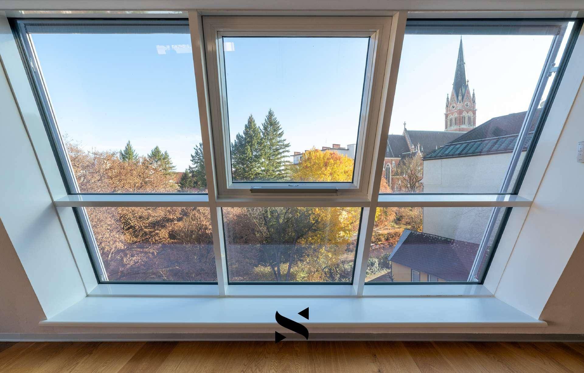 Weitblick aus dem Fenster auf eine Kirche und herbstliche Bäume.