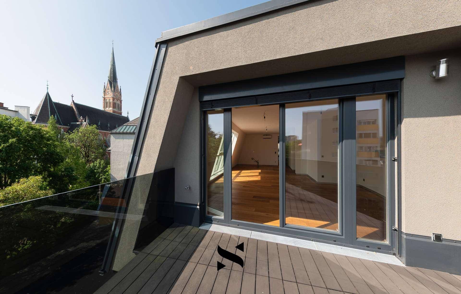 Geräumige Terrasse mit Holzboden und Blick auf die Umgebung und eine Kirche.
