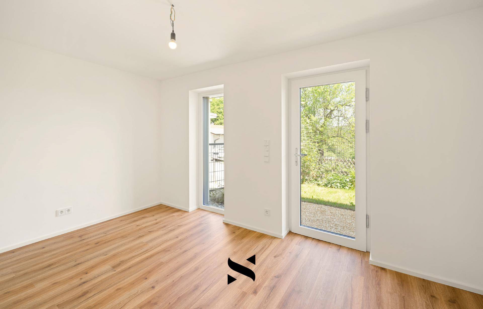 Helles Zimmer mit Laminatboden und Zugang zu einem kleinen Außenbereich oder Garten.