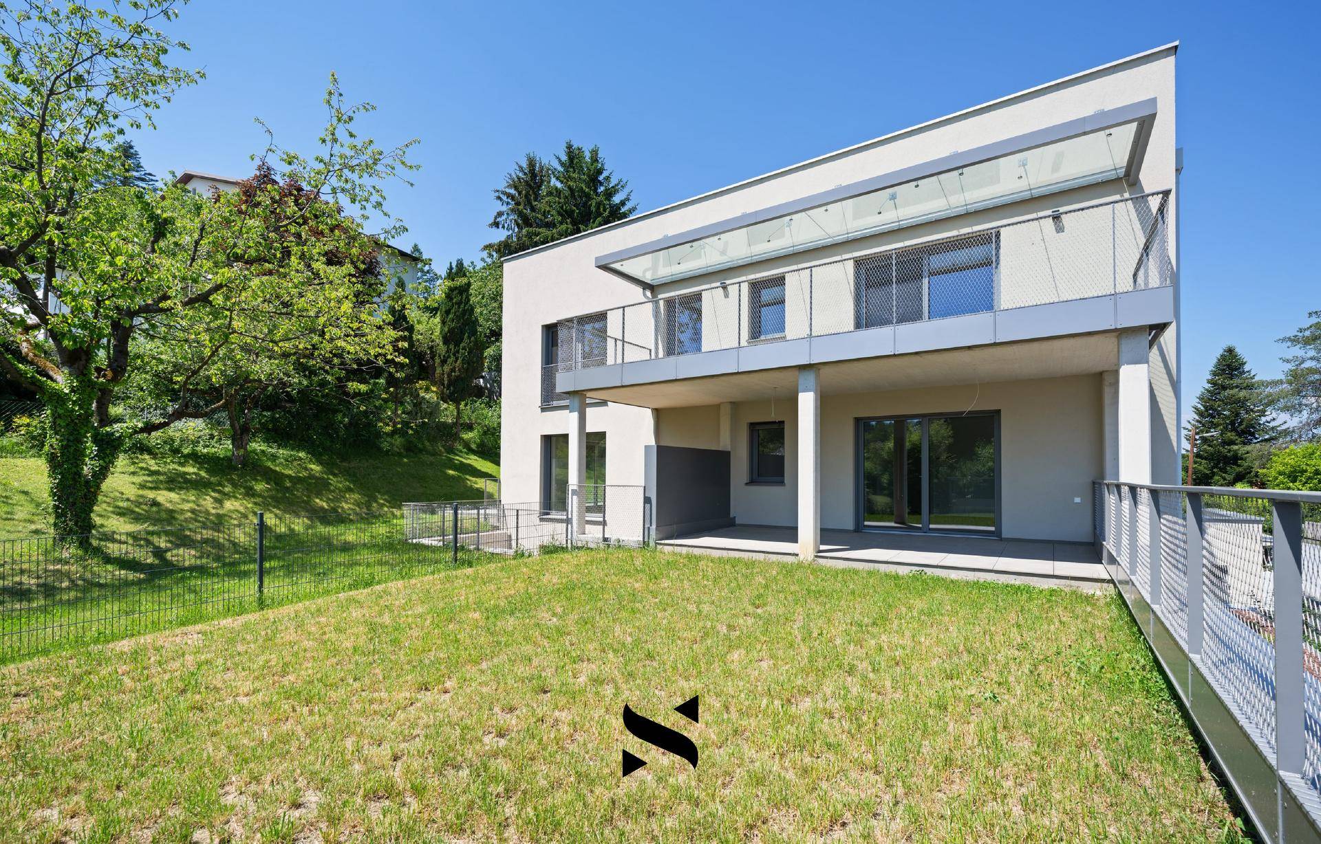 Moderne Hausfassade mit Balkonen und Terrassen, umgeben von einer grünen Landschaft.