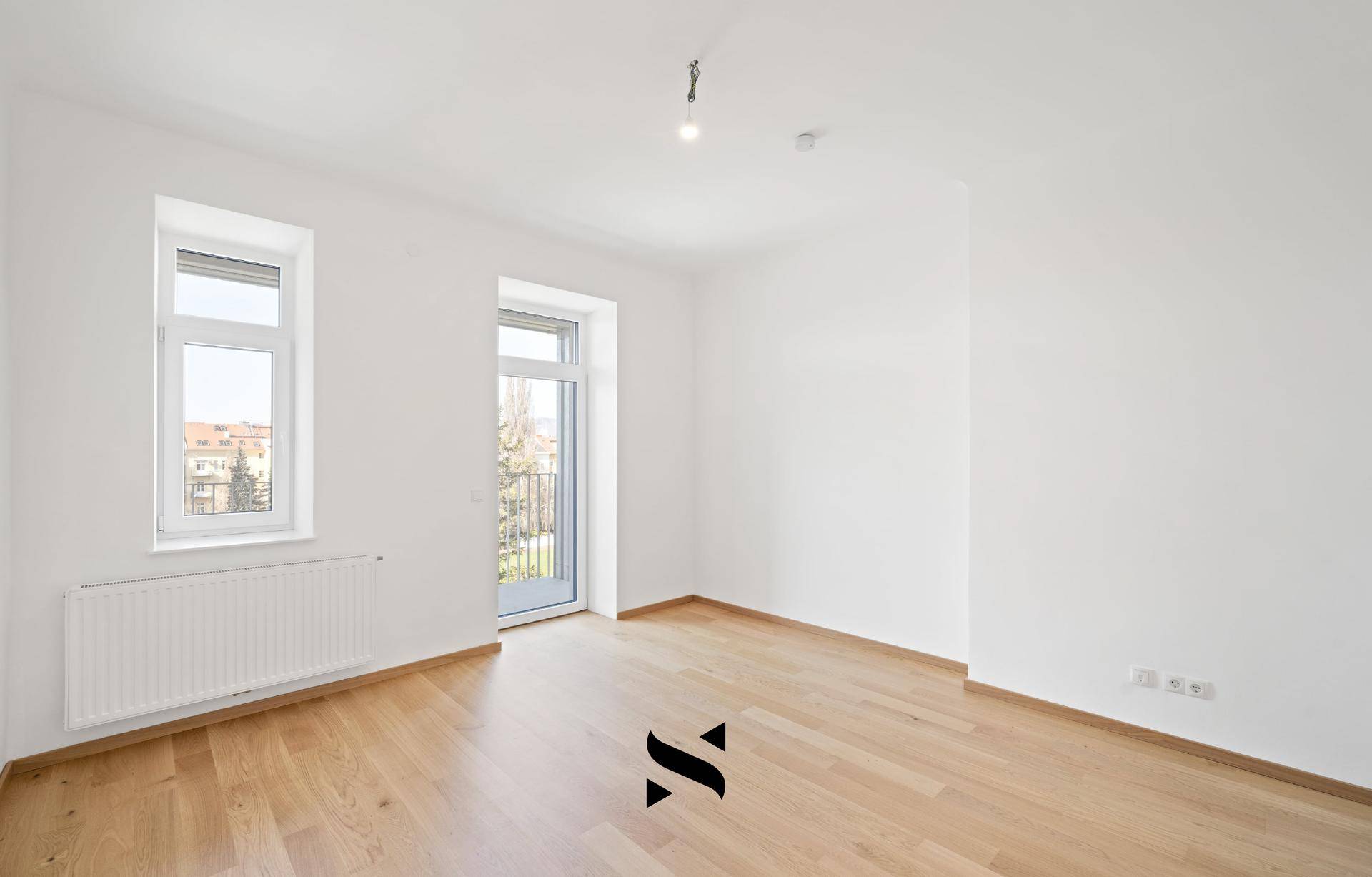 Helles Zimmer mit Parkettboden, weißen Wänden und einem Fenster mit Blick nach draußen.