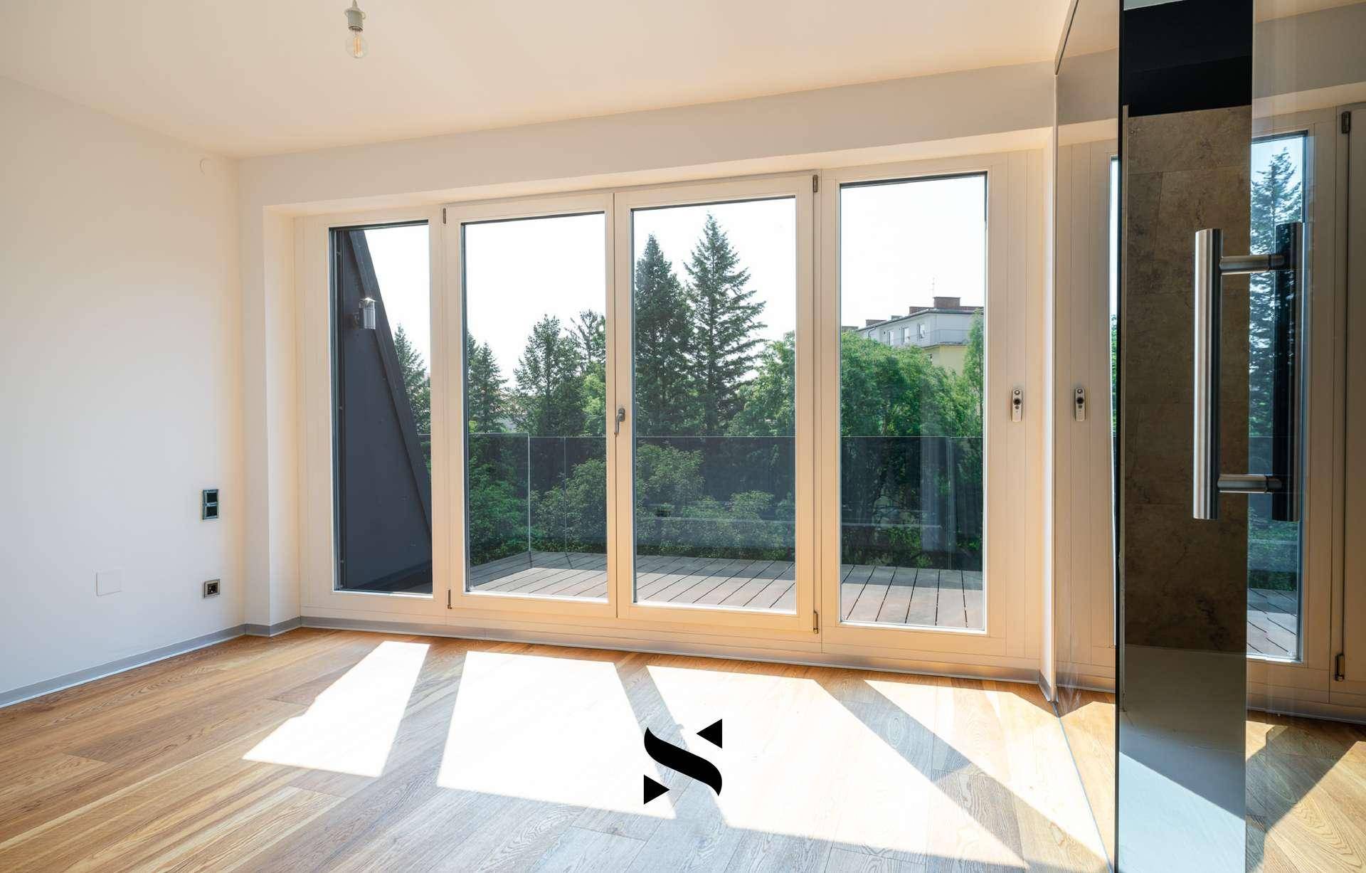 Lichtdurchflutetes Zimmer mit Holzboden und Blick auf Bäume und Grünflächen.