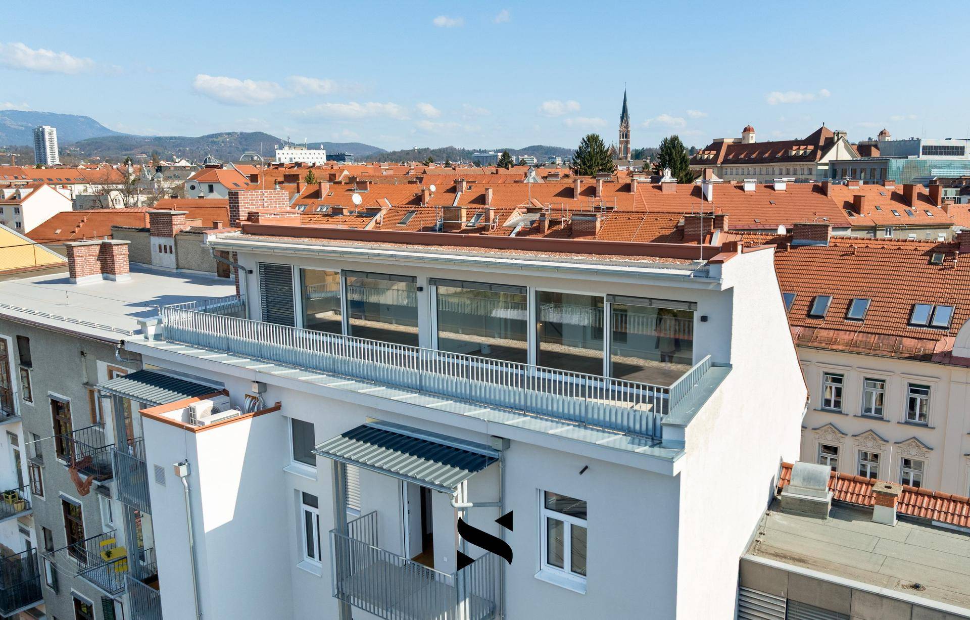 Panoramablick auf ein modernes Gebäude mit weitläufiger Dachterrasse und urbaner Umgebung.
