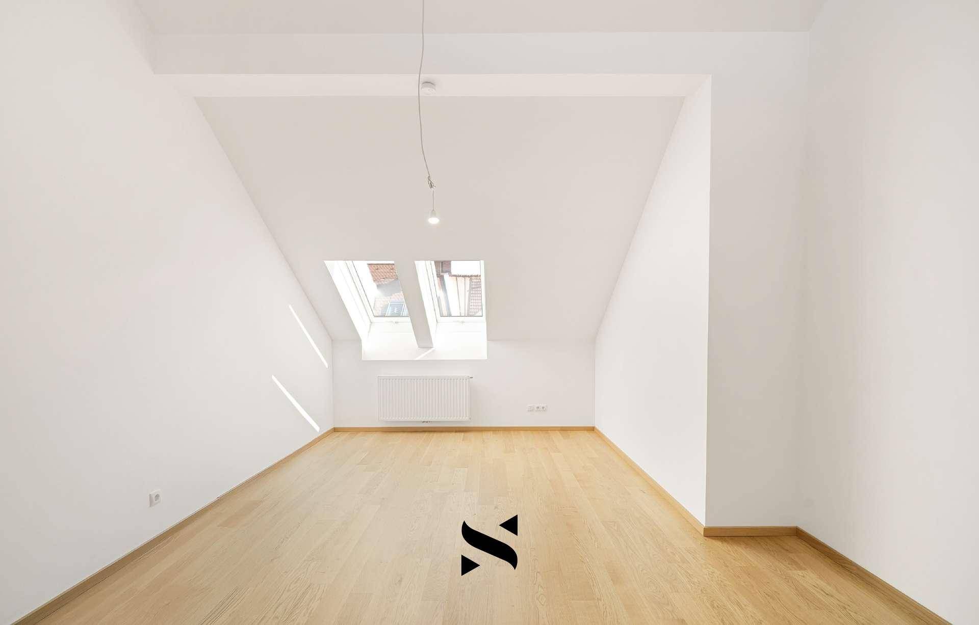 Helles Zimmer im Dachgeschoss mit Holzparkettboden und zwei Dachfenstern.