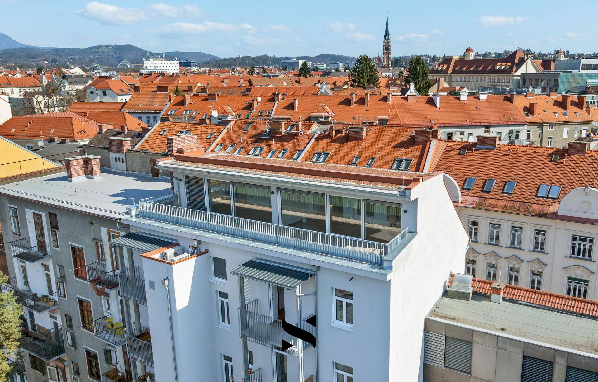 Luftaufnahme eines modernen Gebäudes mit großer Dachterrasse und weitem Blick über die Stadt.