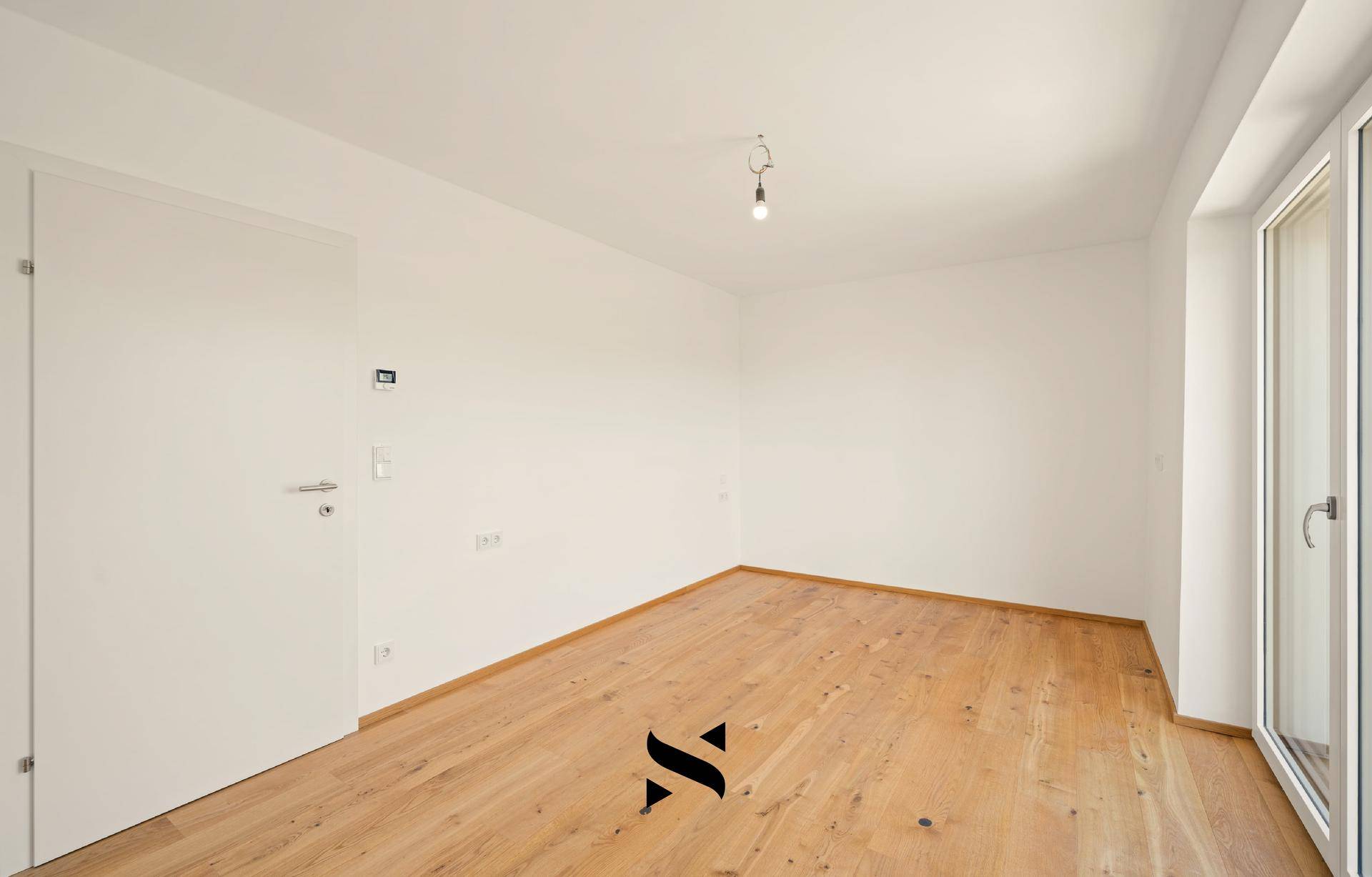 Helles, leeres Zimmer mit Holzboden und einer Tür, bereit für die individuelle Gestaltung.