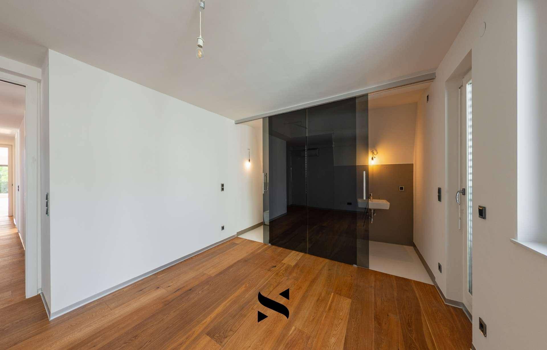 Helles Zimmer mit Holzboden und moderner Glasschiebetür zu einem Badbereich.