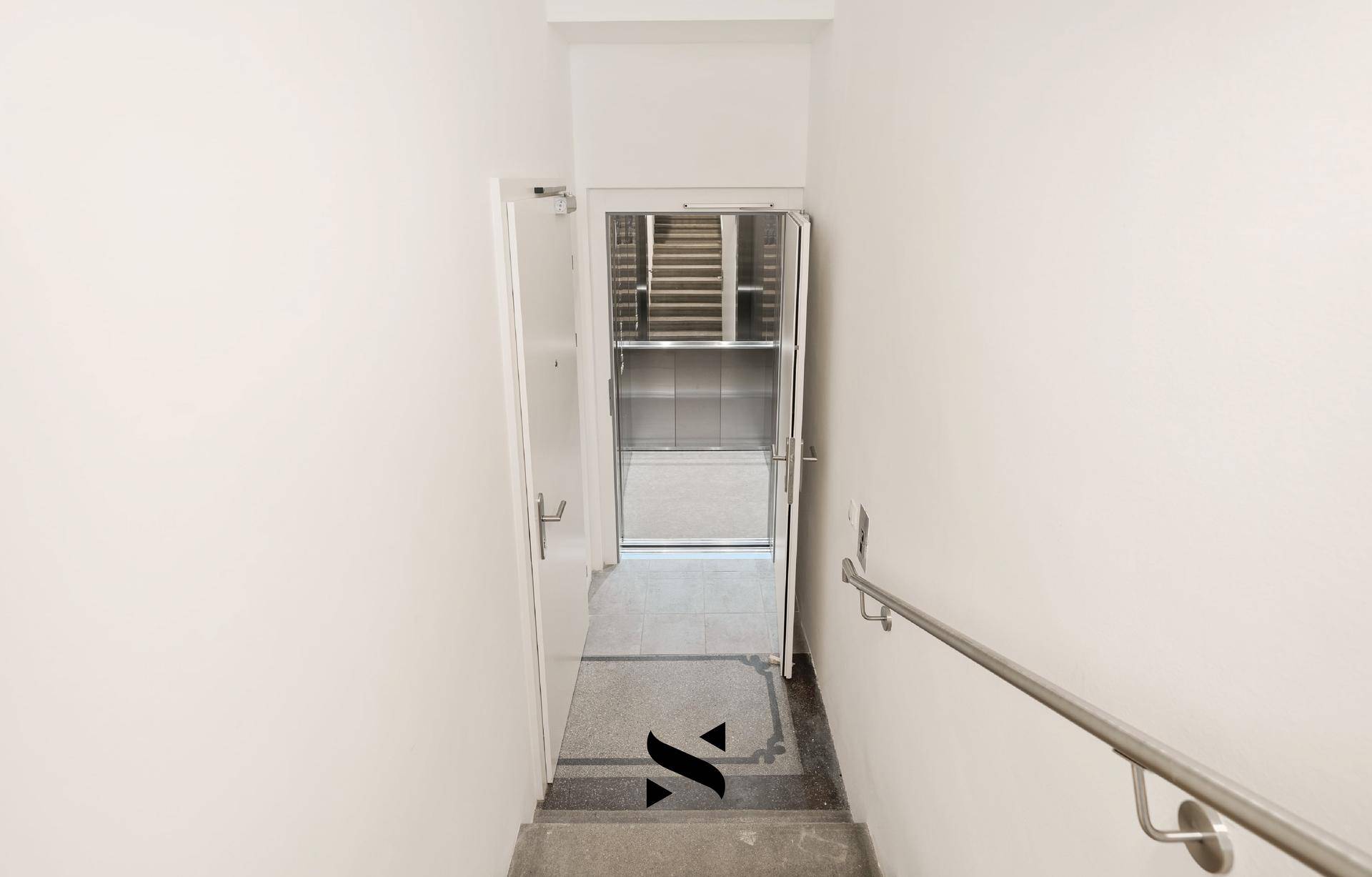 Treppenhaus mit Zugang zu einem modernen Aufzug und Handlauf.