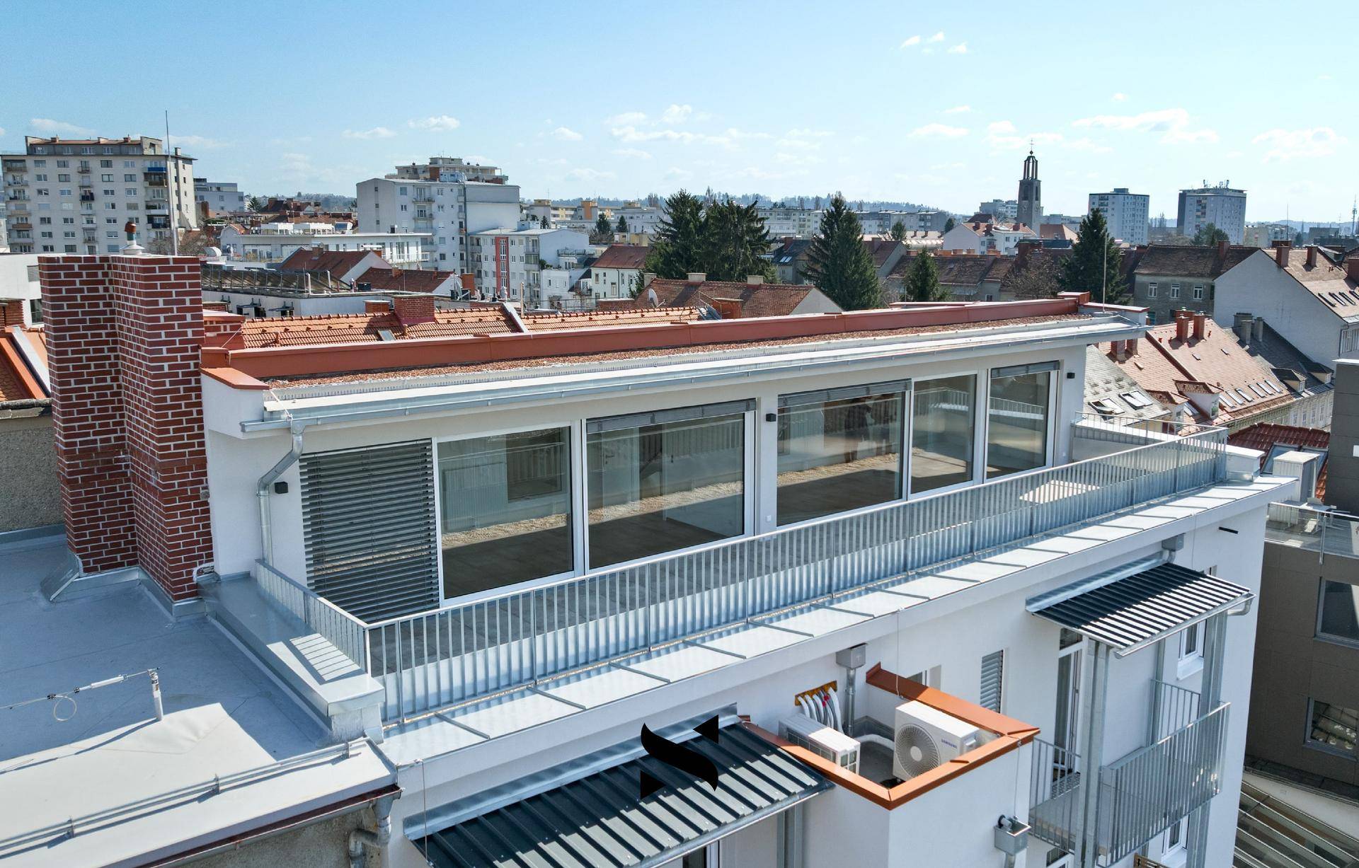 Dachterrasse eines Neubaus mit weitem Blick über die Dächer der Stadt und umliegende Gebäude.