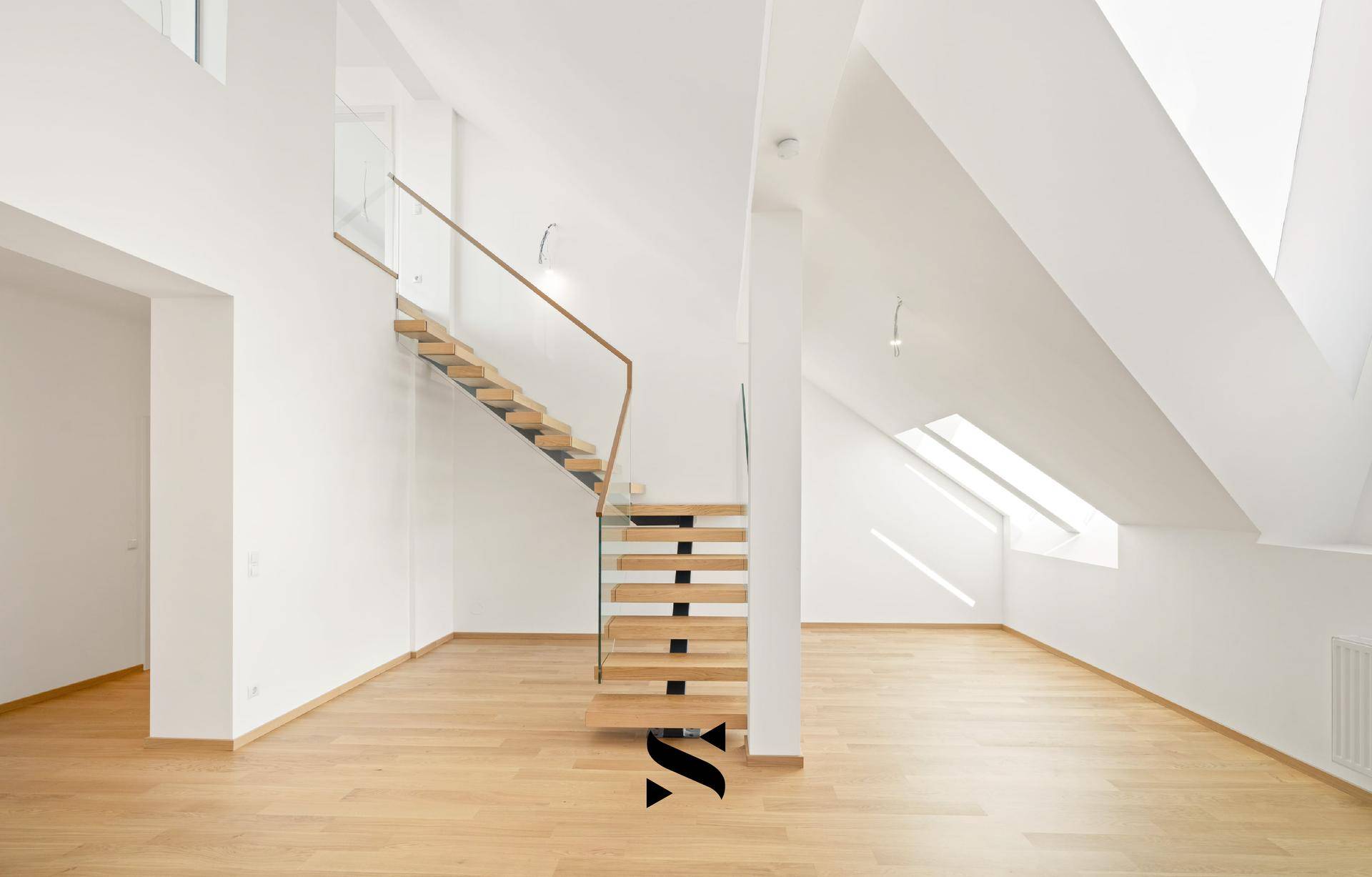 Lichtdurchfluteter Wohnraum mit schwebender Holztreppe, Glasgeländer und Dachschrägen.
