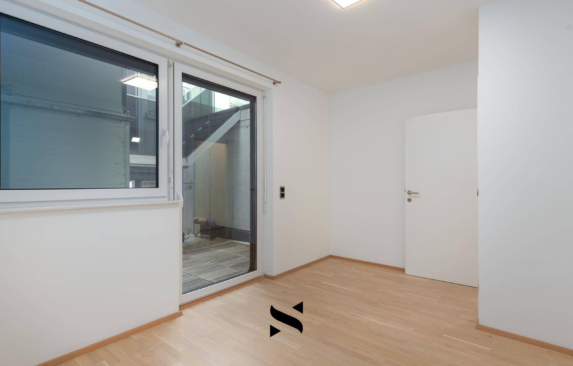 Leeres Zimmer mit Parkettboden und Zugang zu einem kleinen Außenbereich, ideal als Schlafzimmer.