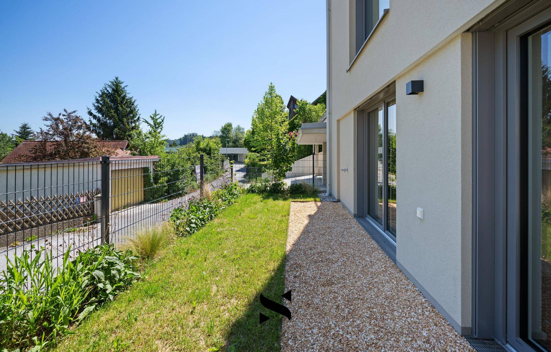 Seitlicher Gartenbereich mit Kiesweg und Rasenfläche entlang der Hausfassade.