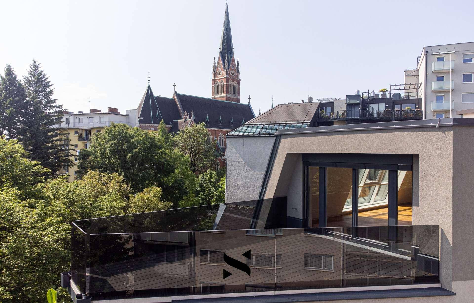 Moderne Dachterrasse mit Glasgeländer und Blick auf die Stadt und eine Kirche.