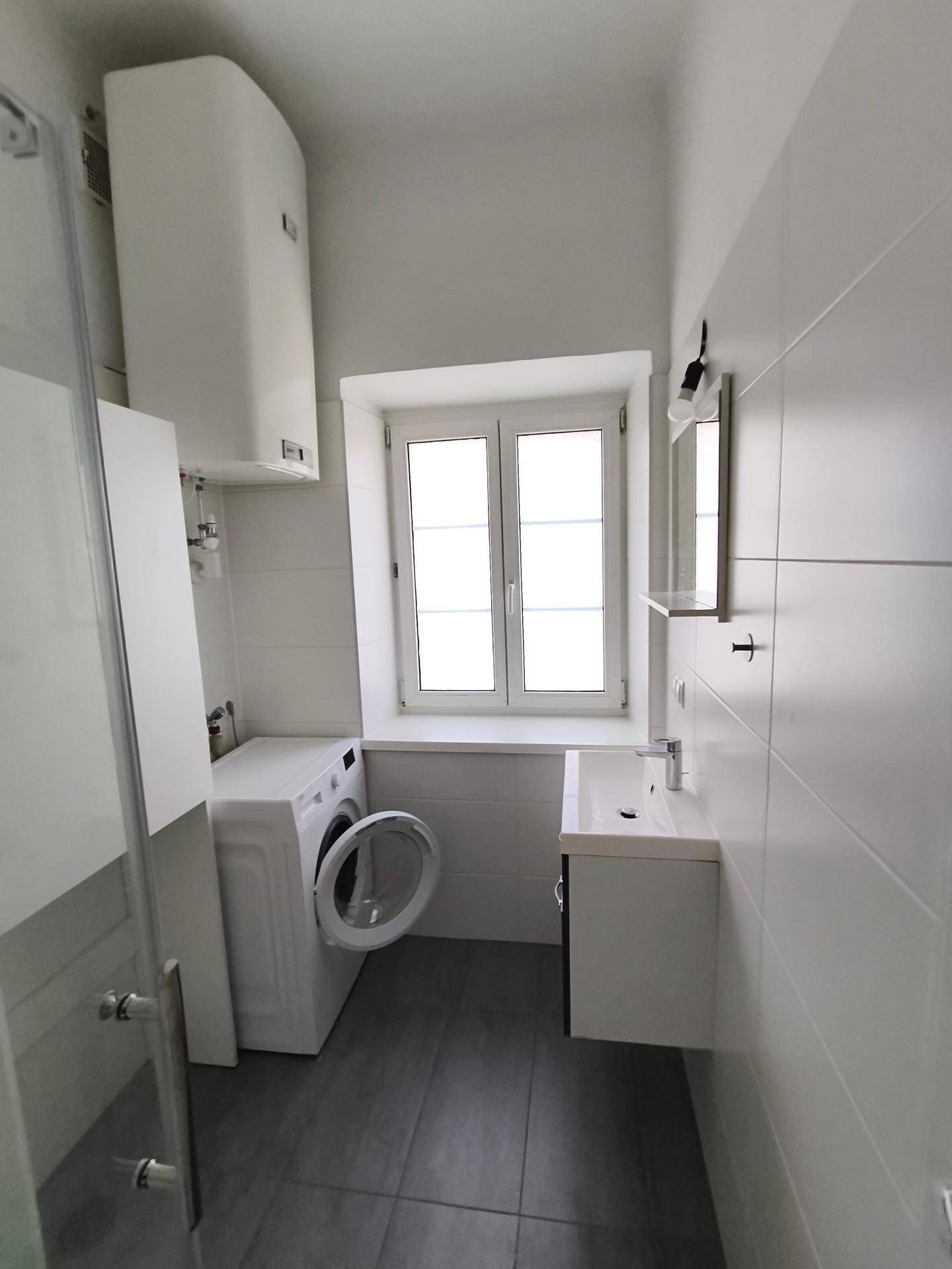 Modernes Badezimmer mit Dusche, Waschbecken, Waschmaschine und Fenster.
