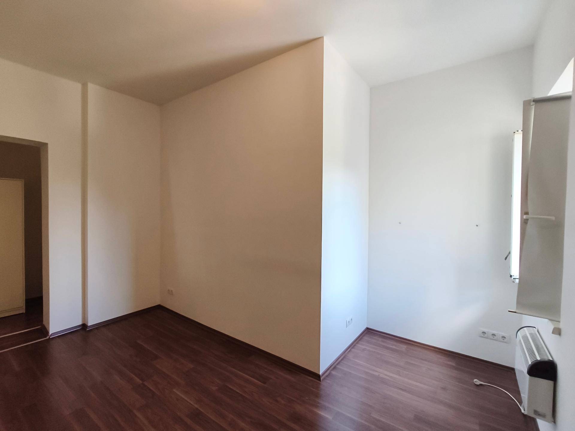 Leeres Zimmer mit dunklem Boden und Fenster, bereit zur individuellen Gestaltung.