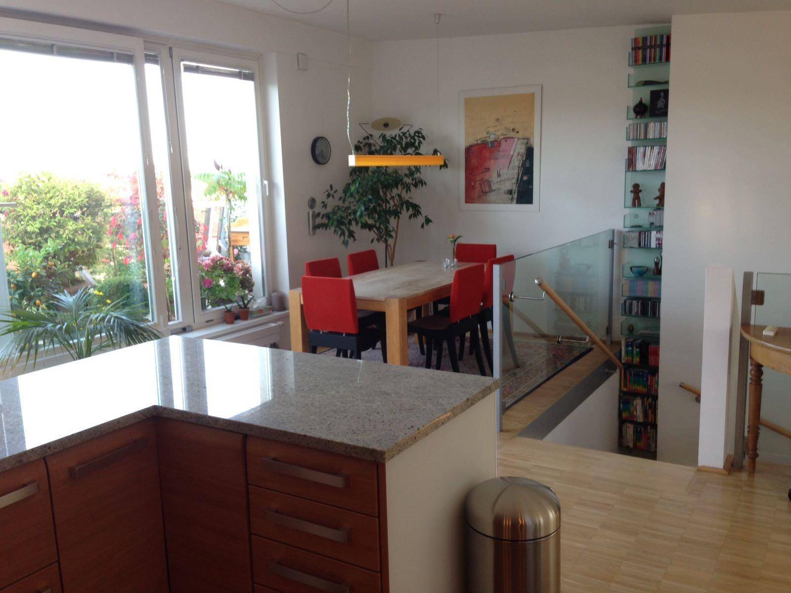 Moderne Küche mit Granitarbeitsplatte und Essbereich, angrenzend an eine Treppe mit Glasgeländer.