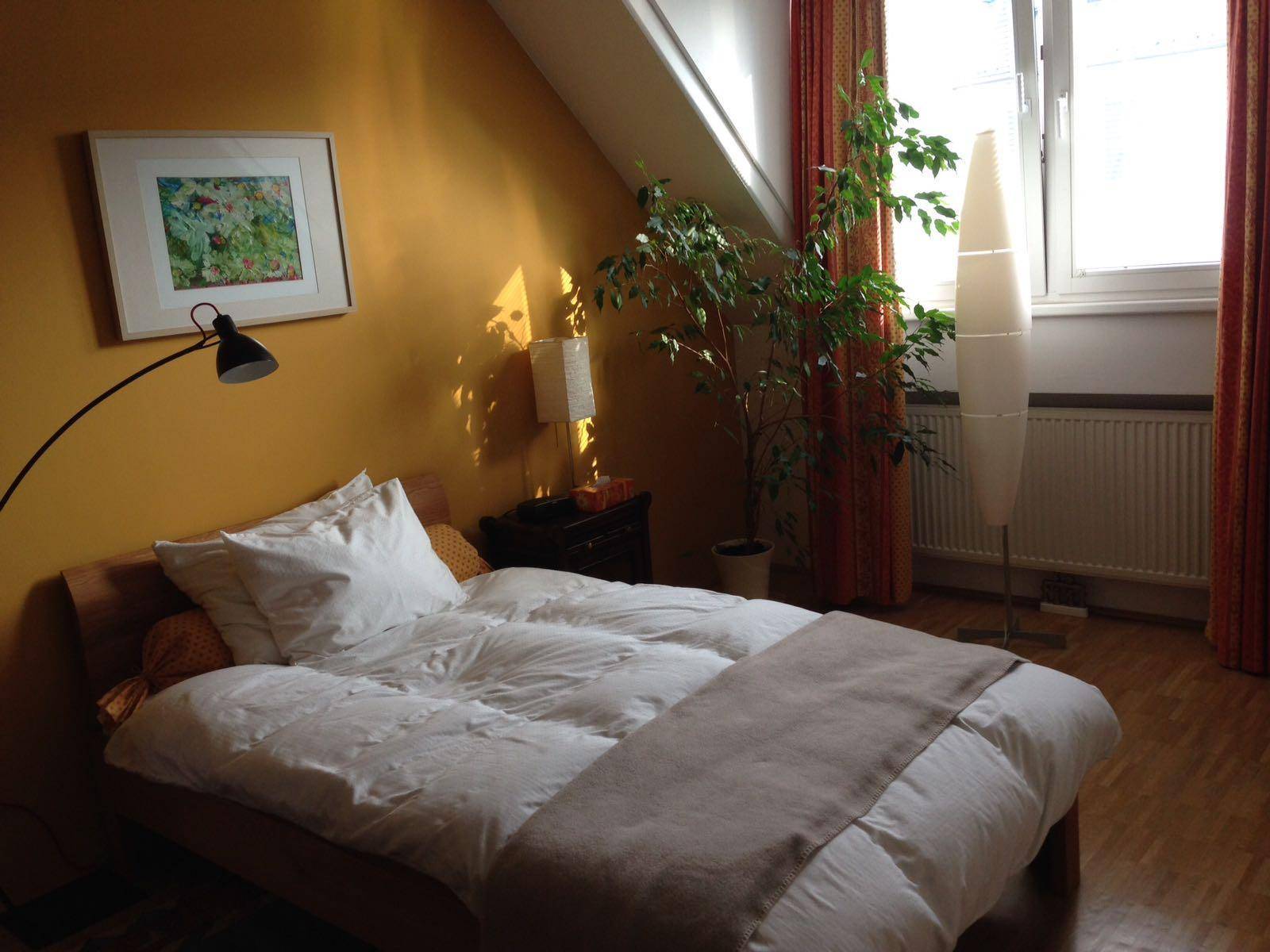 Gemütliches Schlafzimmer im Dachgeschoss mit gelber Wand, Bett und Fenster.