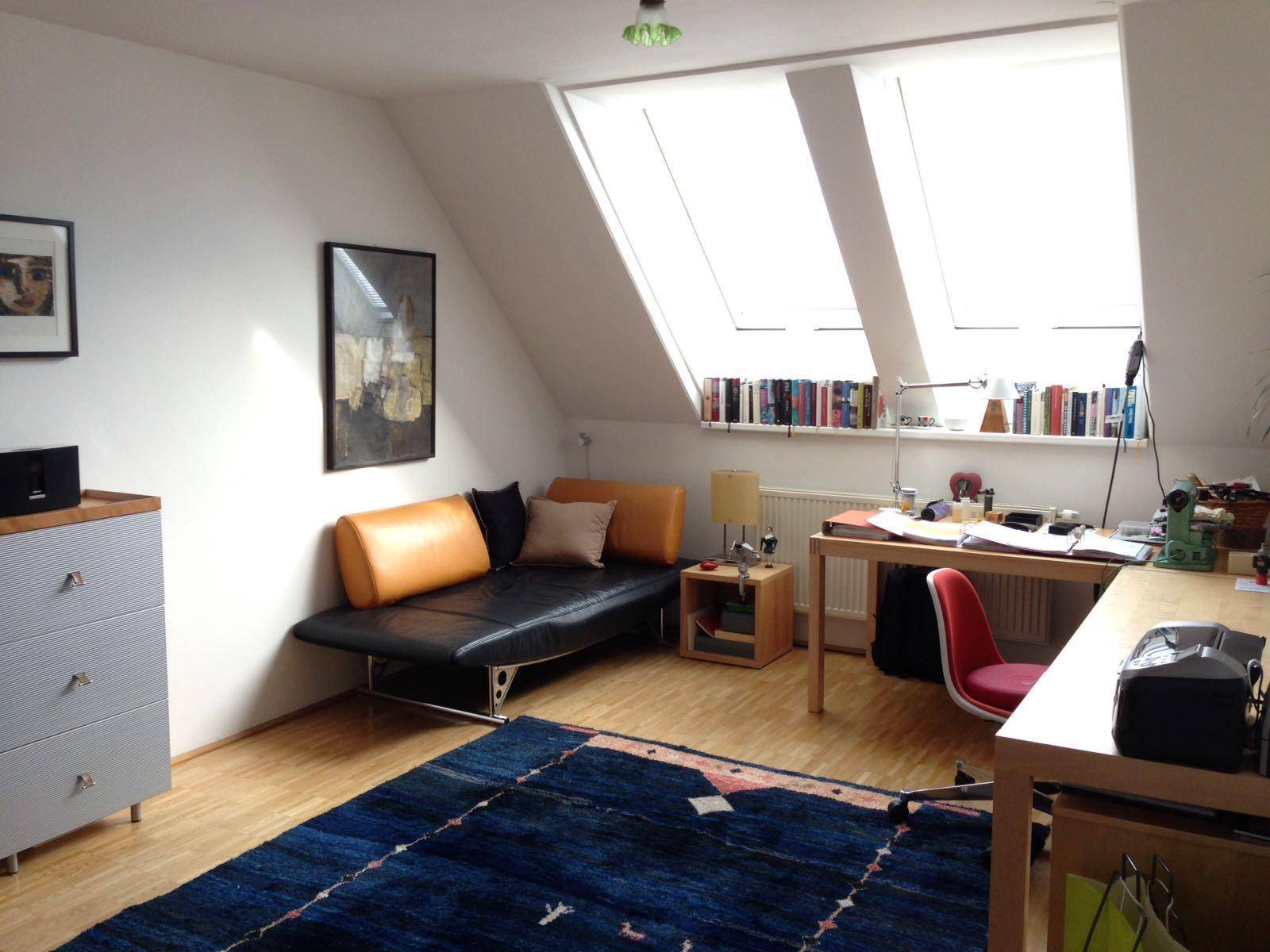 Helles Arbeitszimmer im Dachgeschoss mit Schreibtisch, Sofa und großen Dachfenstern.