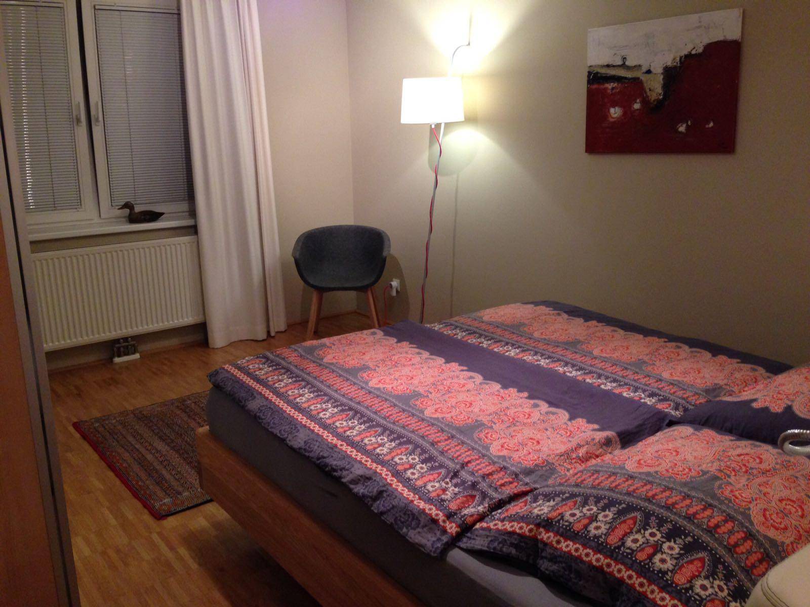 Schlafzimmer mit Fenster, Doppelbett und Holzboden, ausgestattet mit einem Heizkörper.