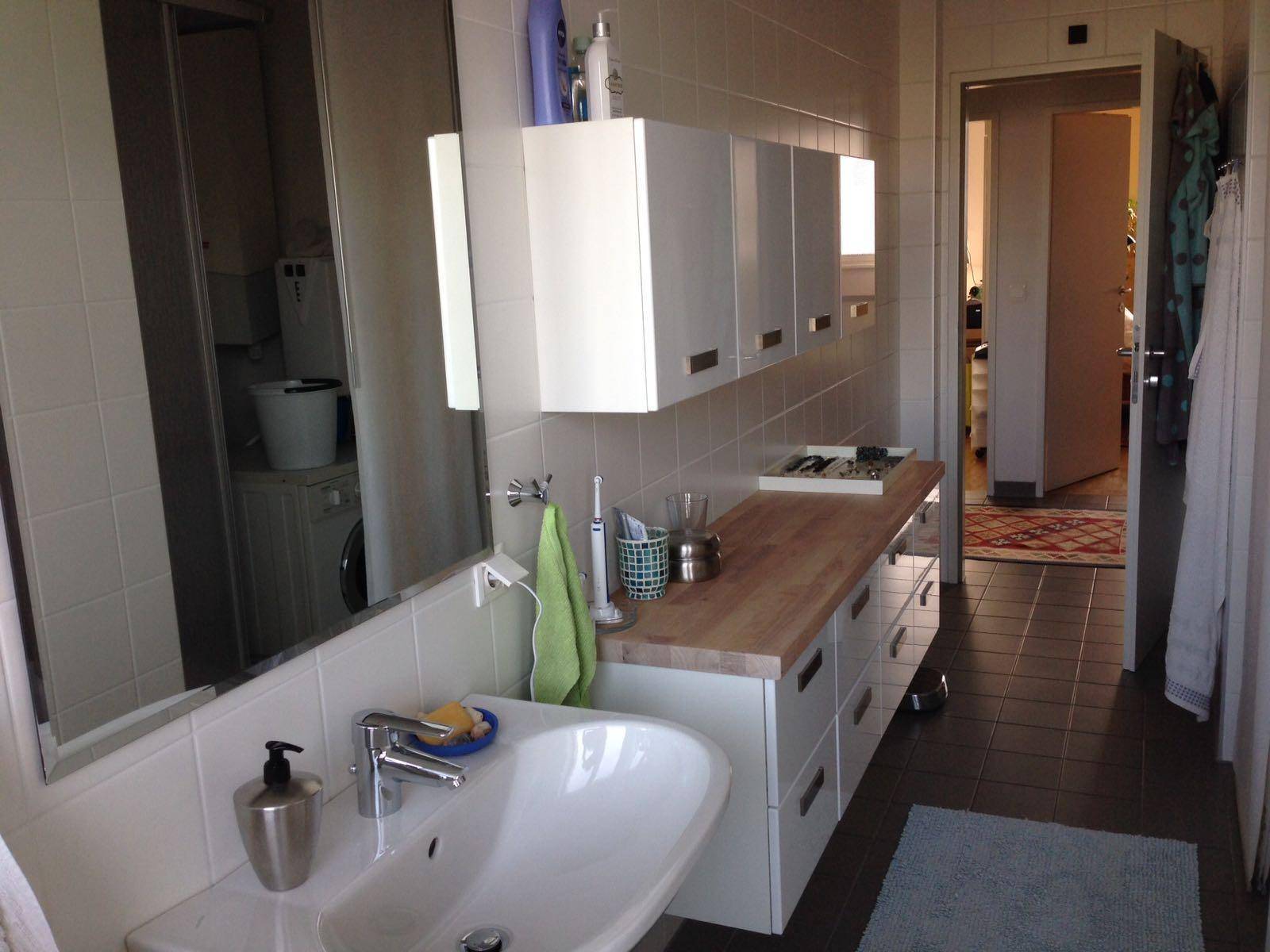 Badezimmer mit Waschbecken, Holzwaschtisch und integrierter Waschmaschine, gefliest.