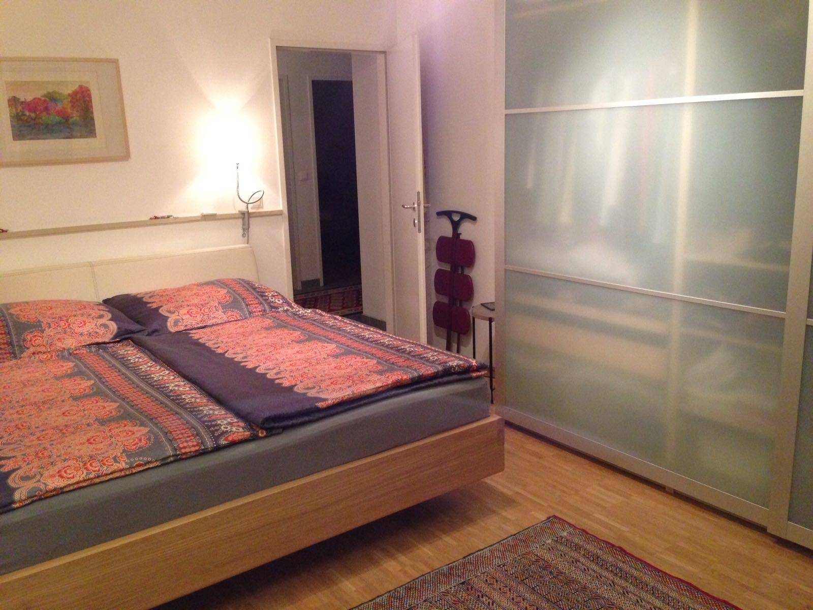 Schlafzimmer mit Doppelbett, Schiebetürenschrank und Holzboden, gut beleuchtet.