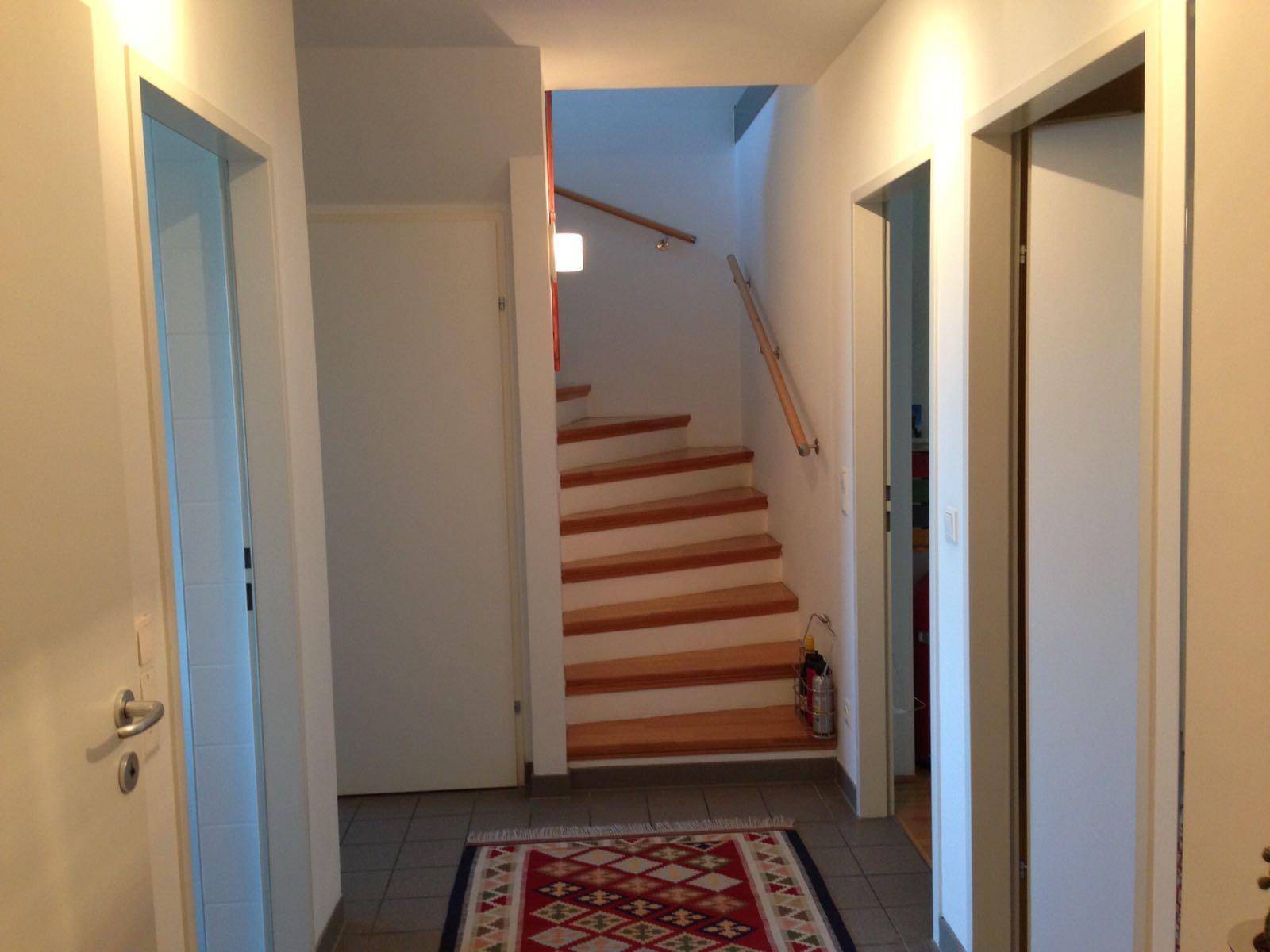 Heller Flur mit Holztreppe, die in die oberen Etagen führt, und Fliesenboden.