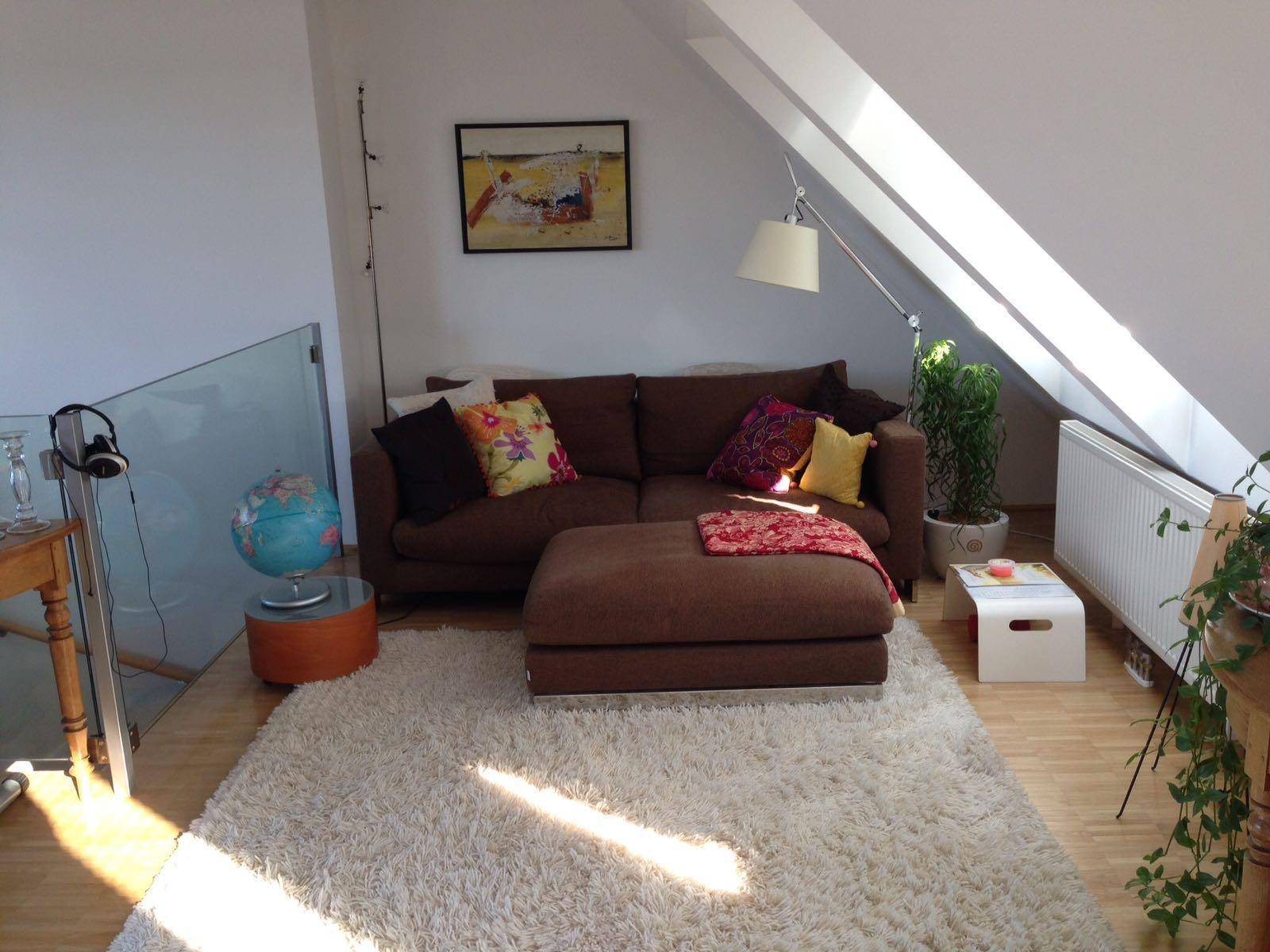 Heller Wohnbereich mit bequemer Couch, Dachschrägen und großem Fenster für viel Tageslicht.