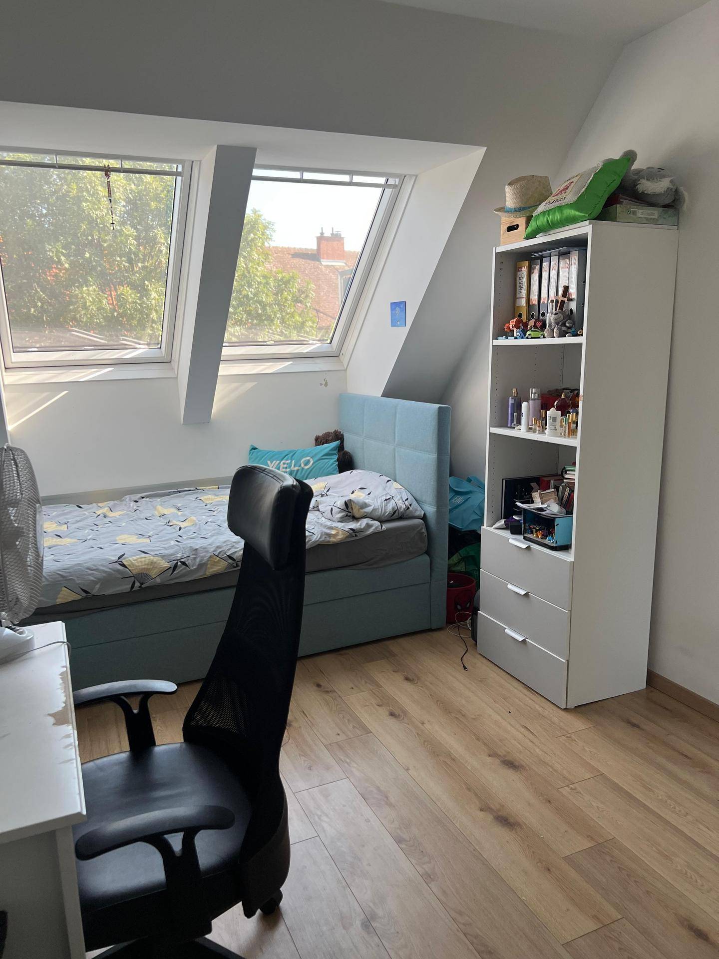 Lichtdurchflutetes Schlafzimmer im Dachgeschoss mit Schreibtisch, Regal und Holzboden.