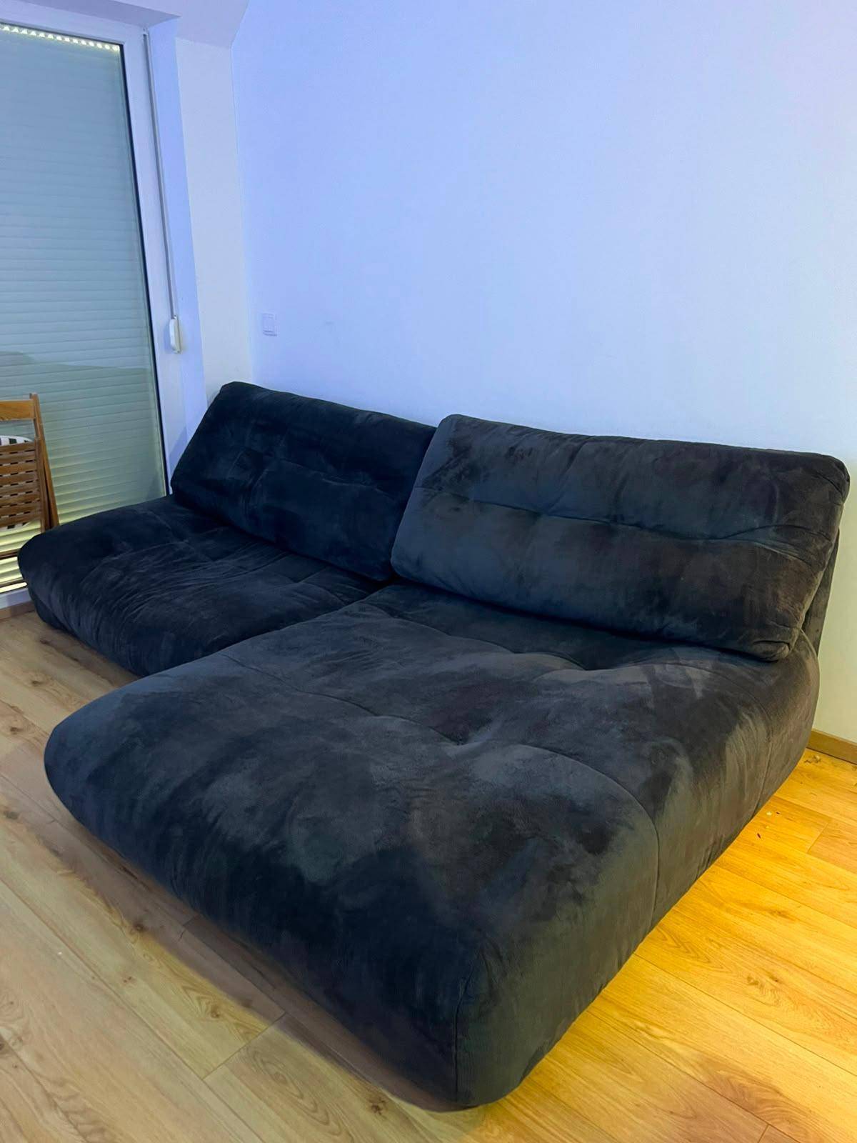 Gemütliches Wohnzimmer mit dunklem Sofa, Holzboden und Zugang zu einem Balkon oder einer Terrasse.