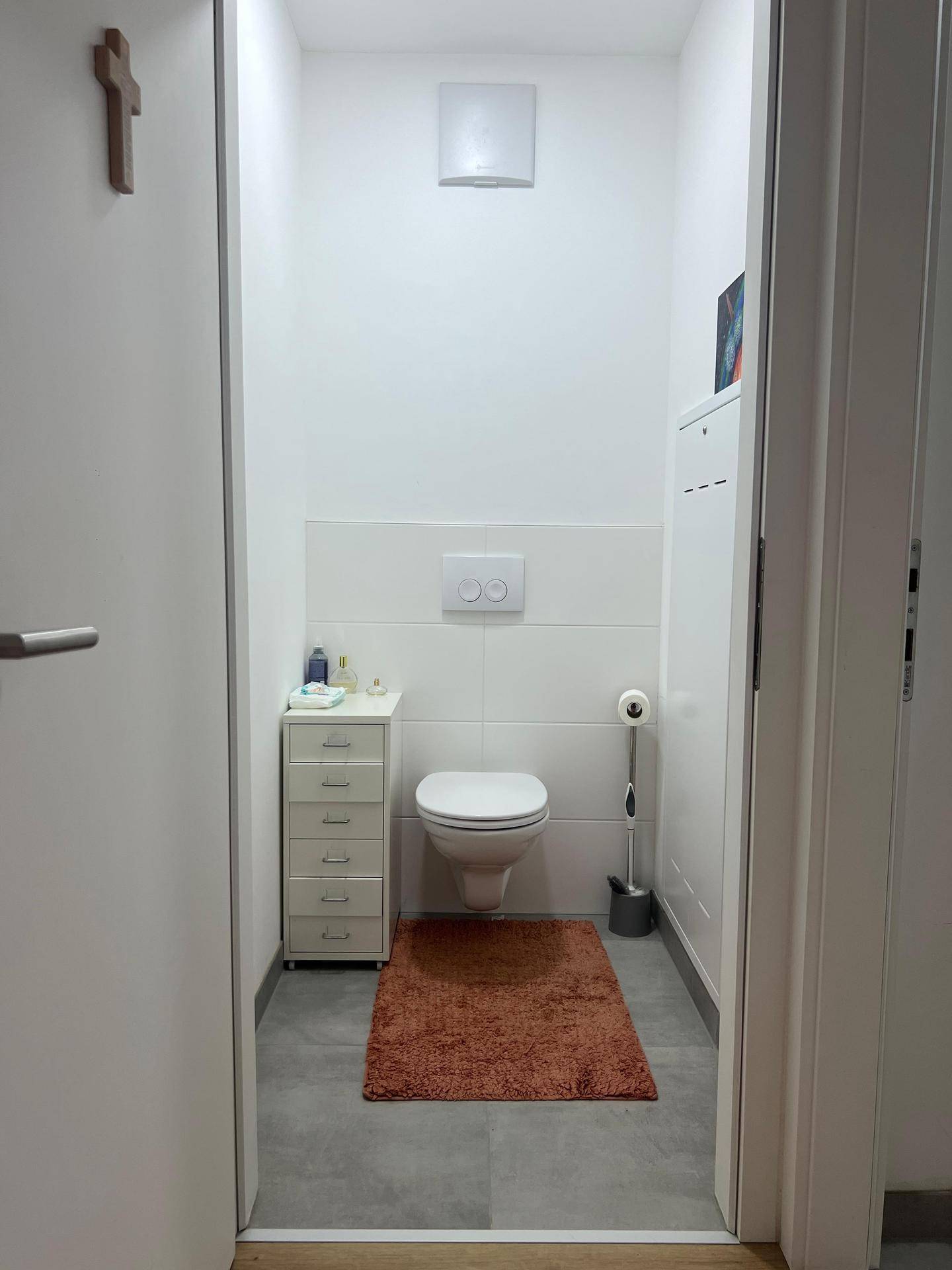 Kleines Gäste-WC mit wandhängender Toilette, Fliesenboden und einem kleinen Beistellschrank.