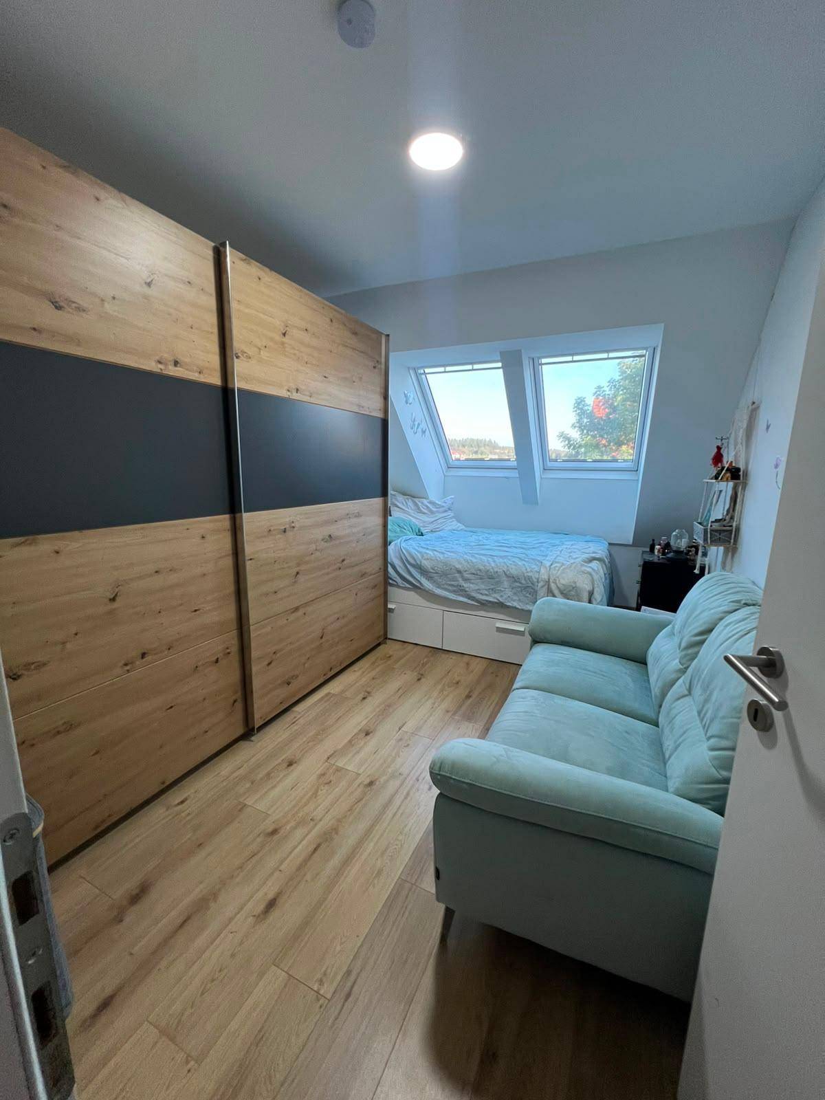 Helles Schlafzimmer im Dachgeschoss mit großen Dachfenstern, Holzboden und Einbauschrank.