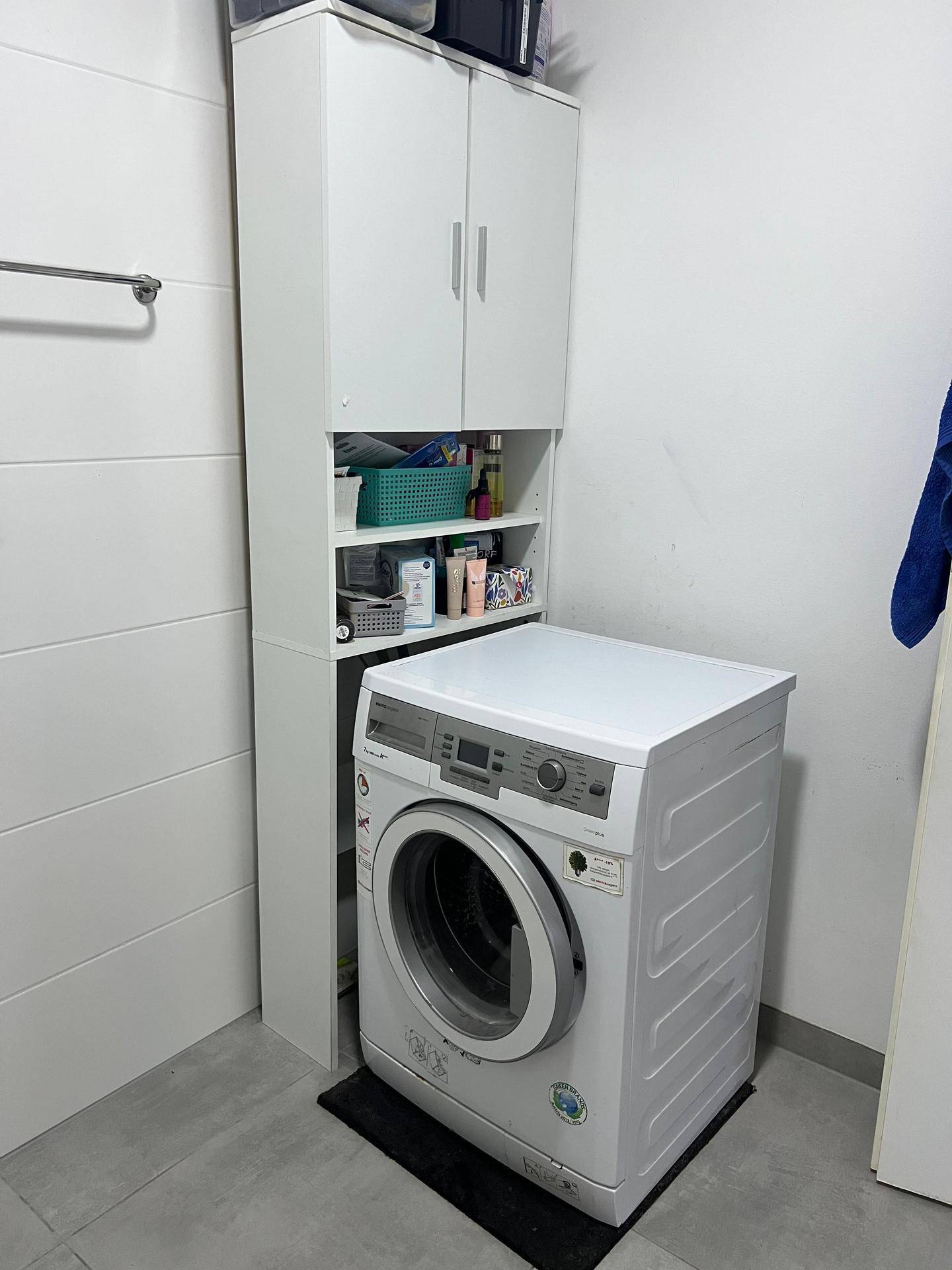 Praktischer Waschbereich mit Waschmaschine und hohem Stauraumschrank auf Fliesenboden.