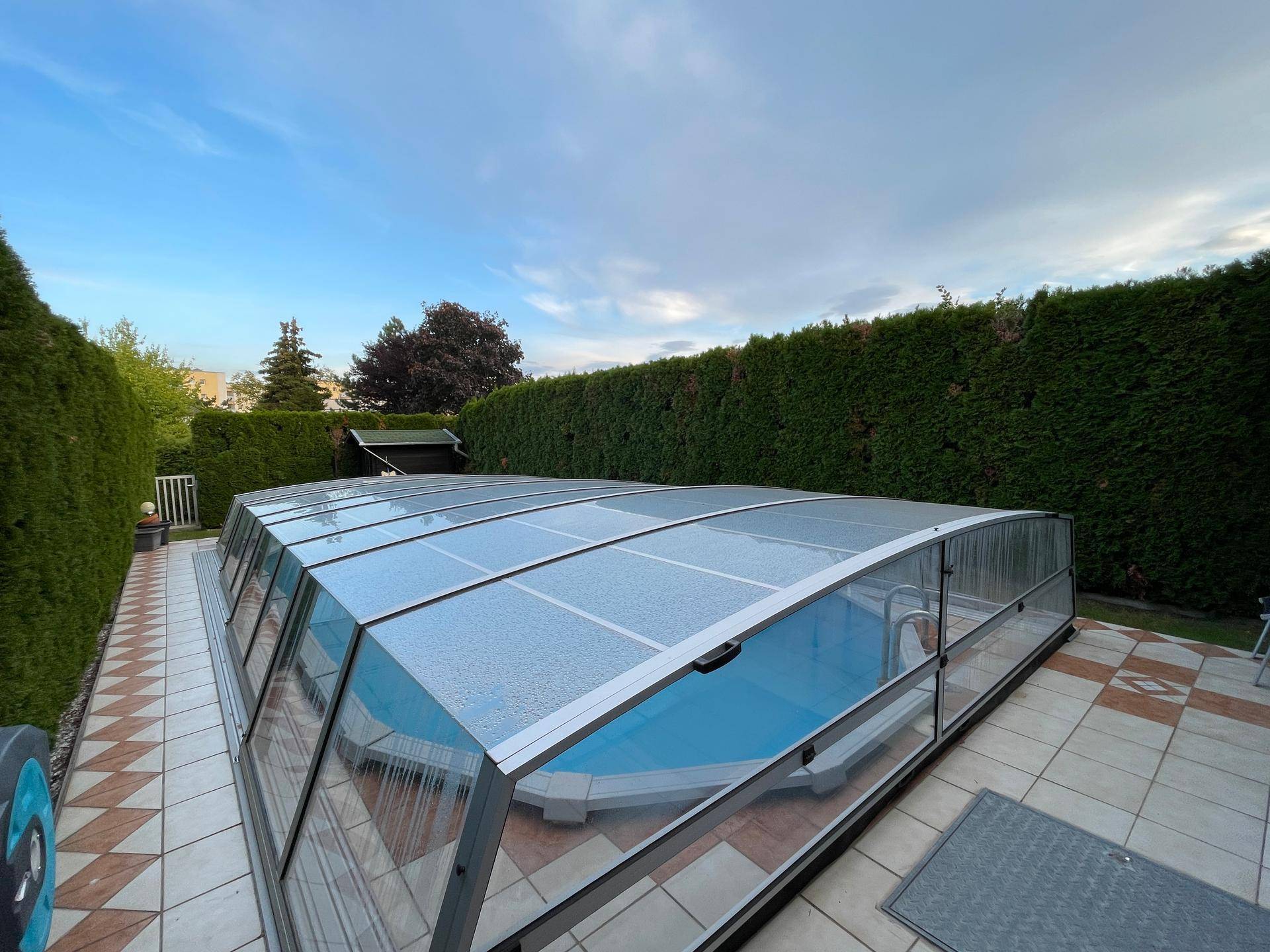 Terrasse mit Fliesenboden und einem modernen, überdachten Swimmingpool, umgeben von hohen Hecken.