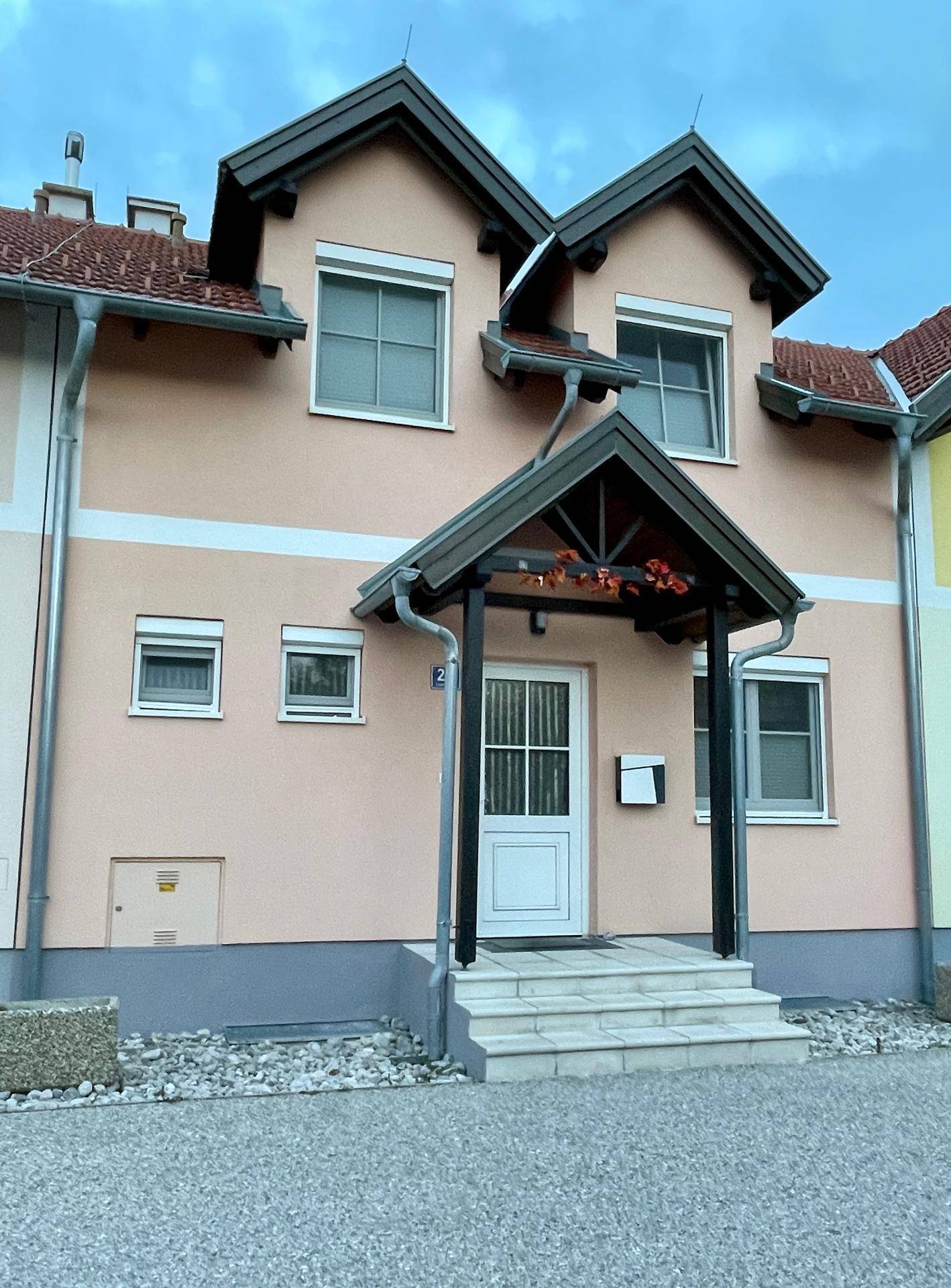 Vorderansicht eines modernen Einfamilienhauses mit hellrosa Fassade und überdachtem Eingangsbereich.