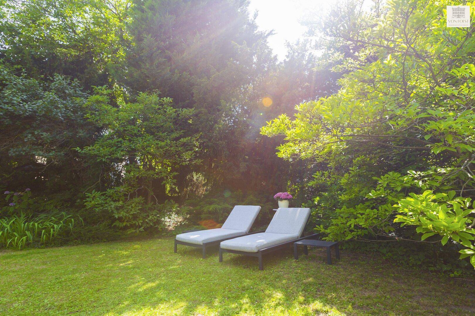 Zwei moderne Sonnenliegen auf der grünen Rasenfläche, umgeben von üppiger, sonniger Vegetation.