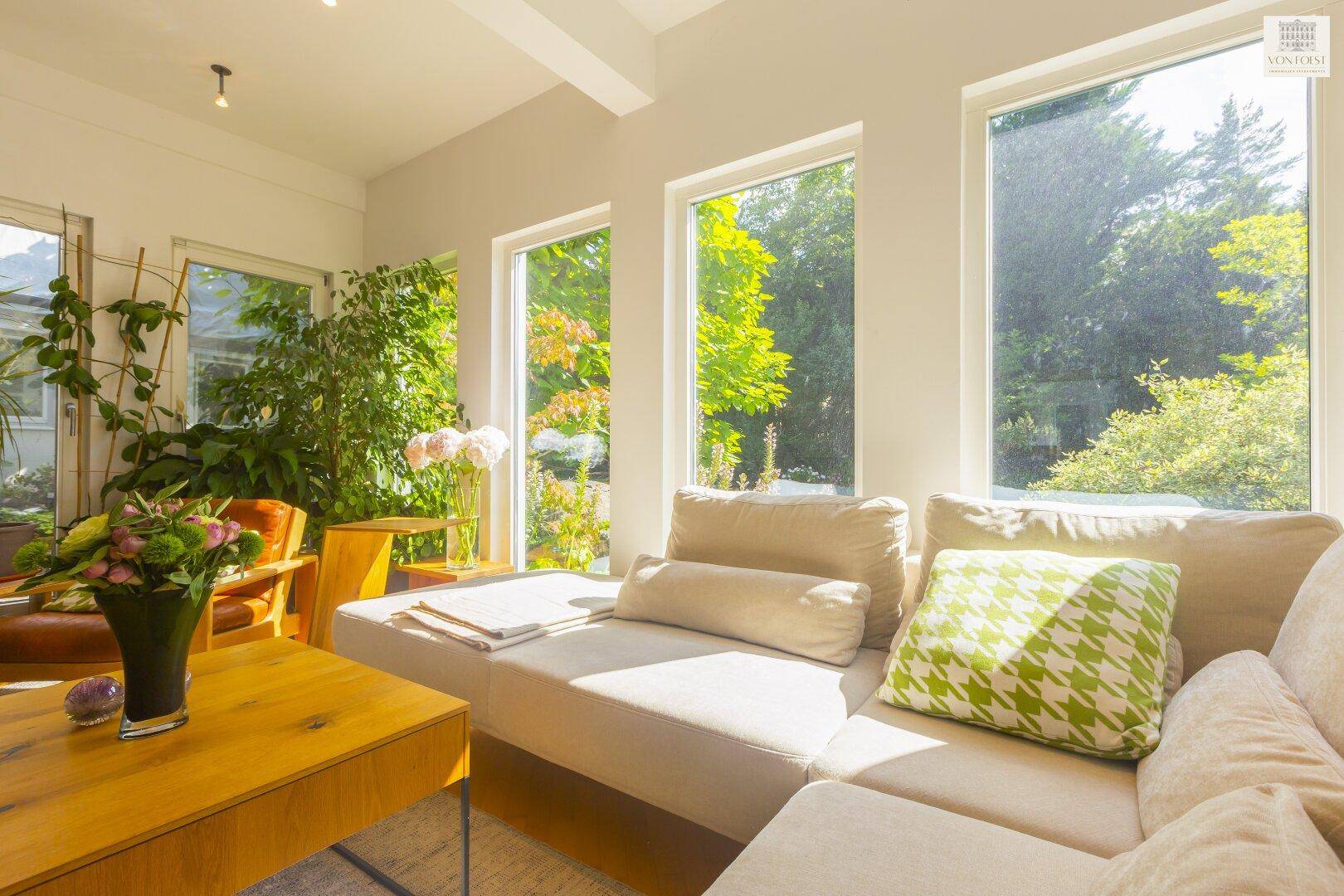 Helles Wohnzimmer mit beigem Sofa, Holztisch und großen Fenstern mit Blick ins Grüne.