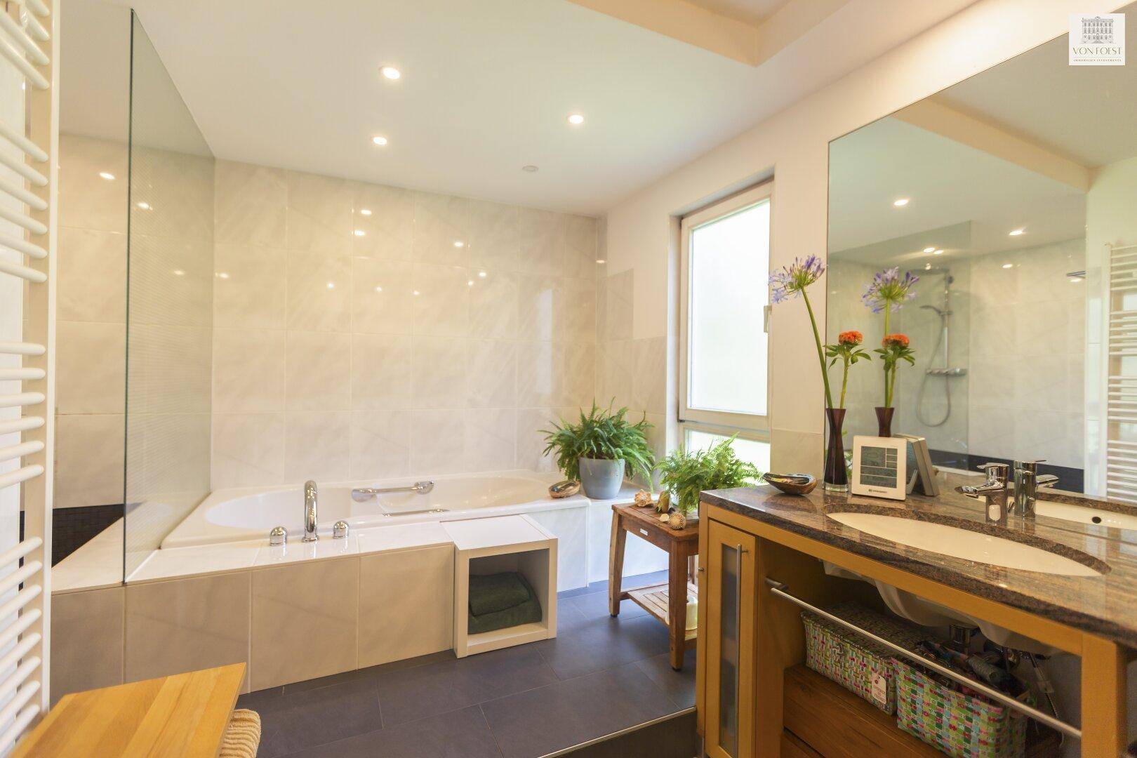 Modernes Badezimmer mit Badewanne, Doppelwaschbecken und großem Spiegel, hell gefliest.