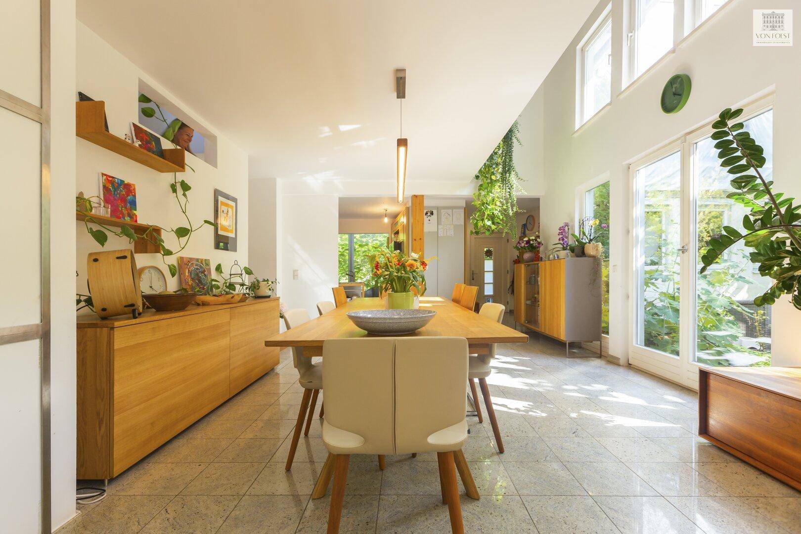 Moderner Essbereich mit Holztisch, hellen Stühlen und großen Fenstern zum Garten.