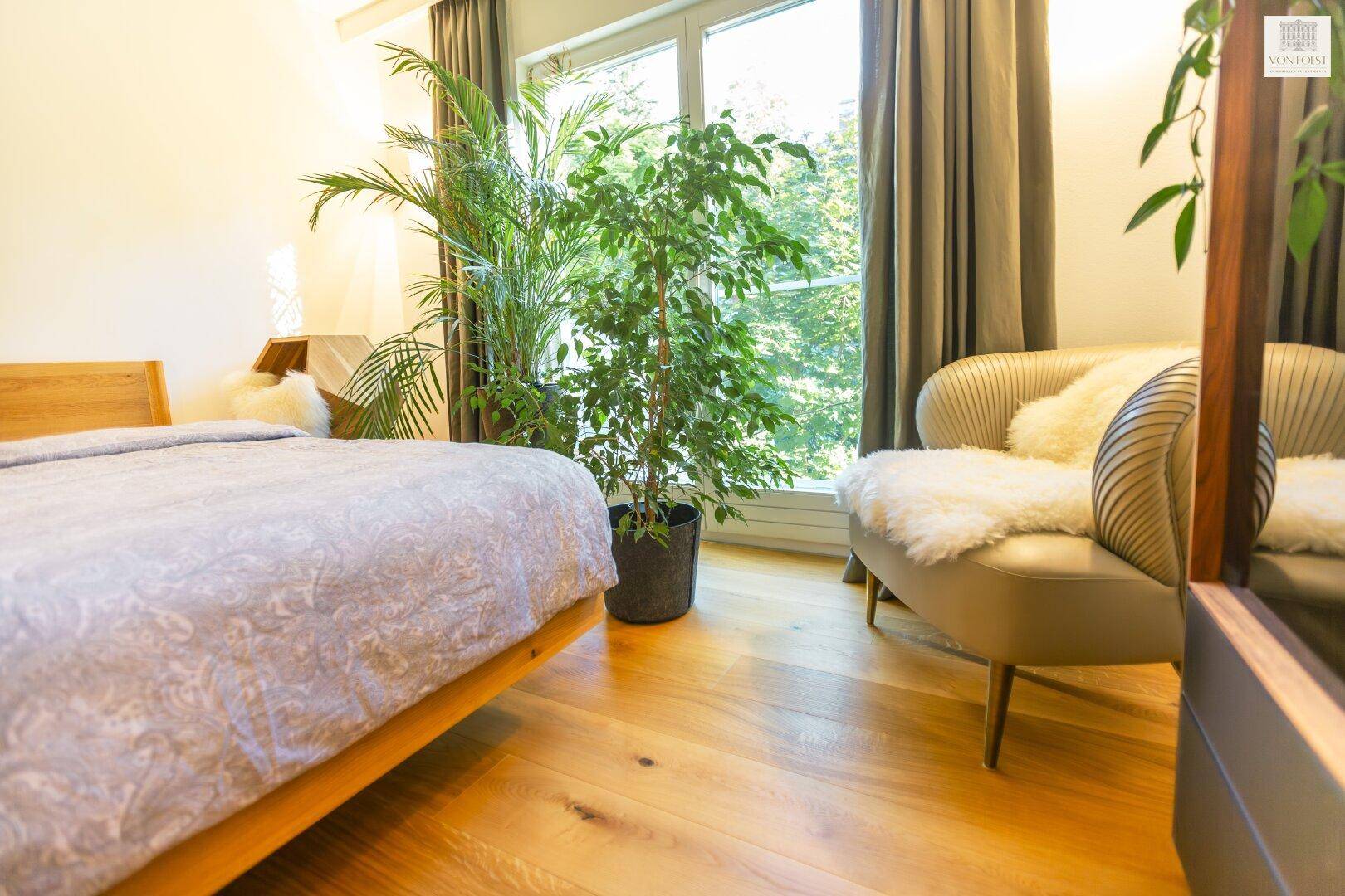 Helles Schlafzimmer mit Holzboden, großem Fenster und Pflanzen, gemütlich eingerichtet.