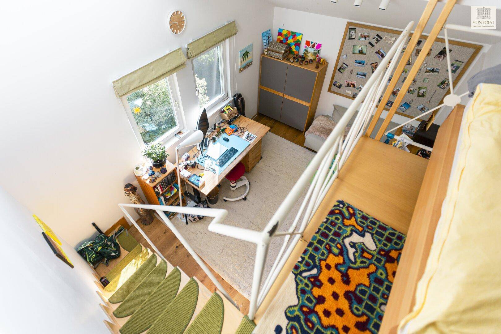 Blick von oben auf ein helles Kinderzimmer mit Hochbett, Schreibtisch und Teppichboden.