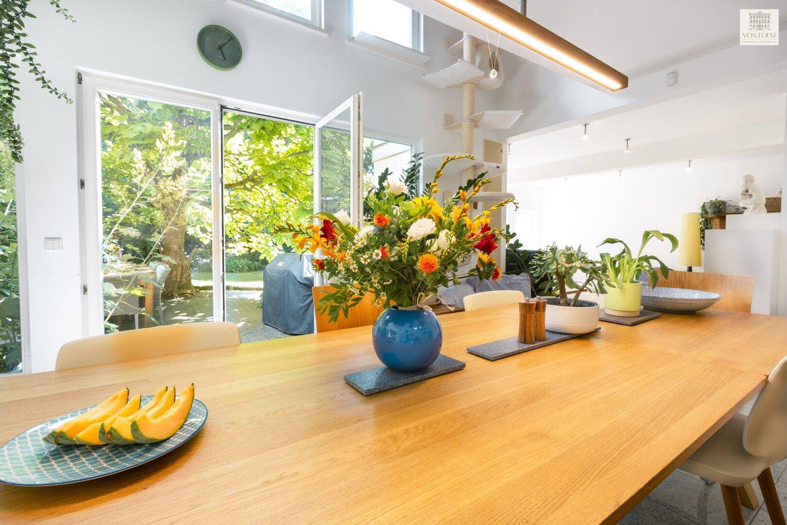 Großer Holzesstisch mit frischen Blumen und Obst, umgeben von natürlichem Licht.