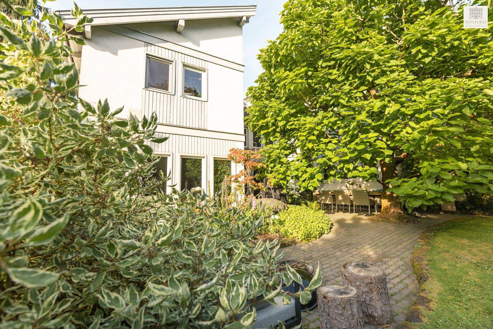Seitlicher Blick auf das moderne Haus mit gepflegtem Garten, Sträuchern und einem großen Baum.