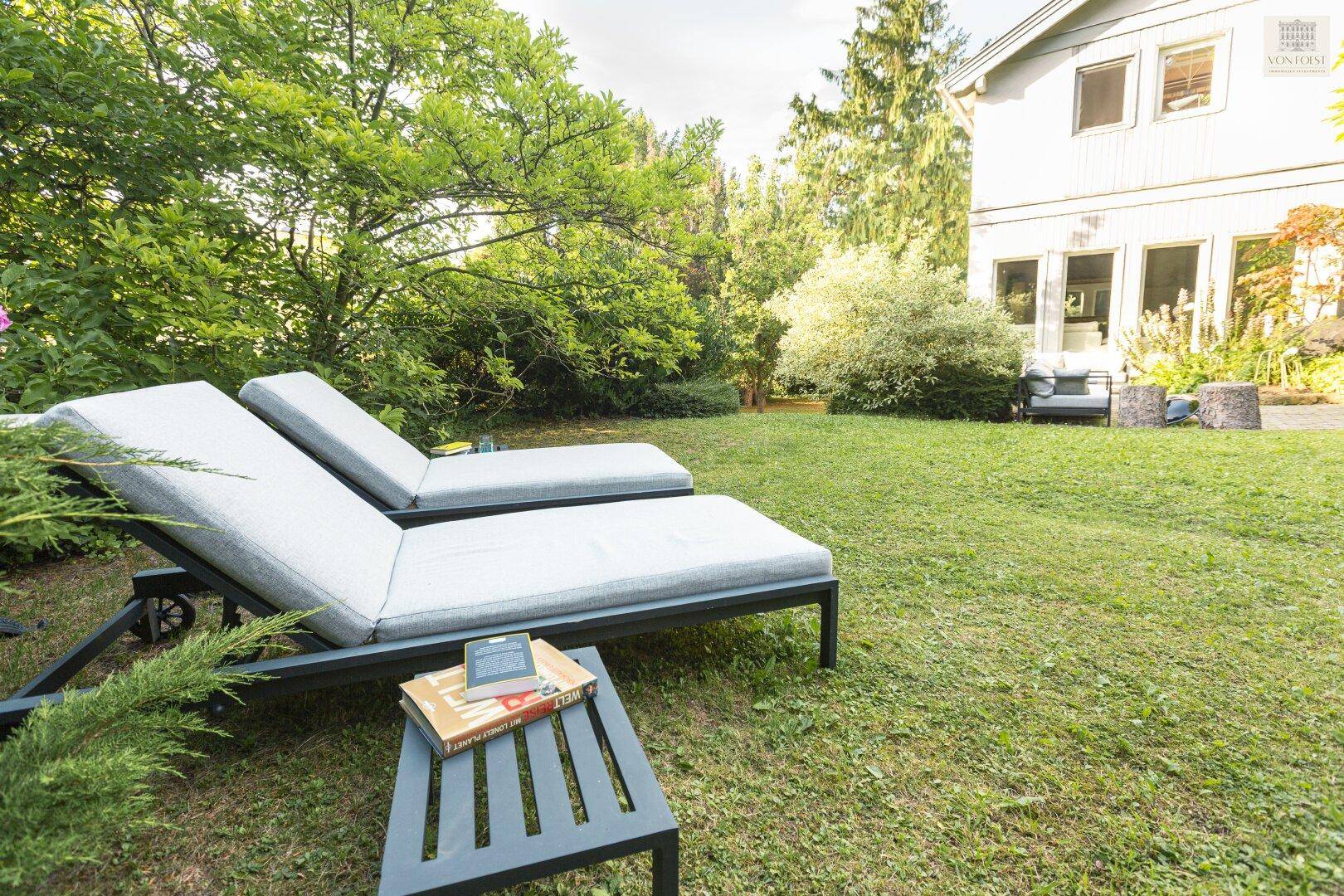 Entspannungsbereich im Garten mit Sonnenliegen und Blick auf die moderne Architektur des Hauses.