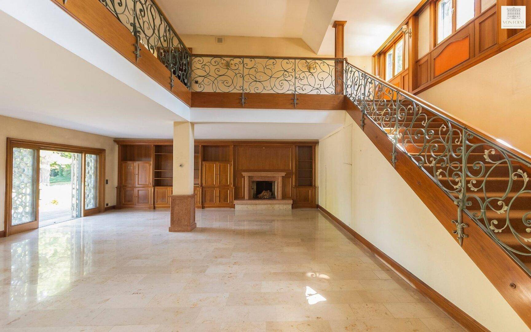 Eleganter Wohnbereich mit imposanter Treppe, Kamin und maßgefertigten Holzregalen auf Marmorboden.